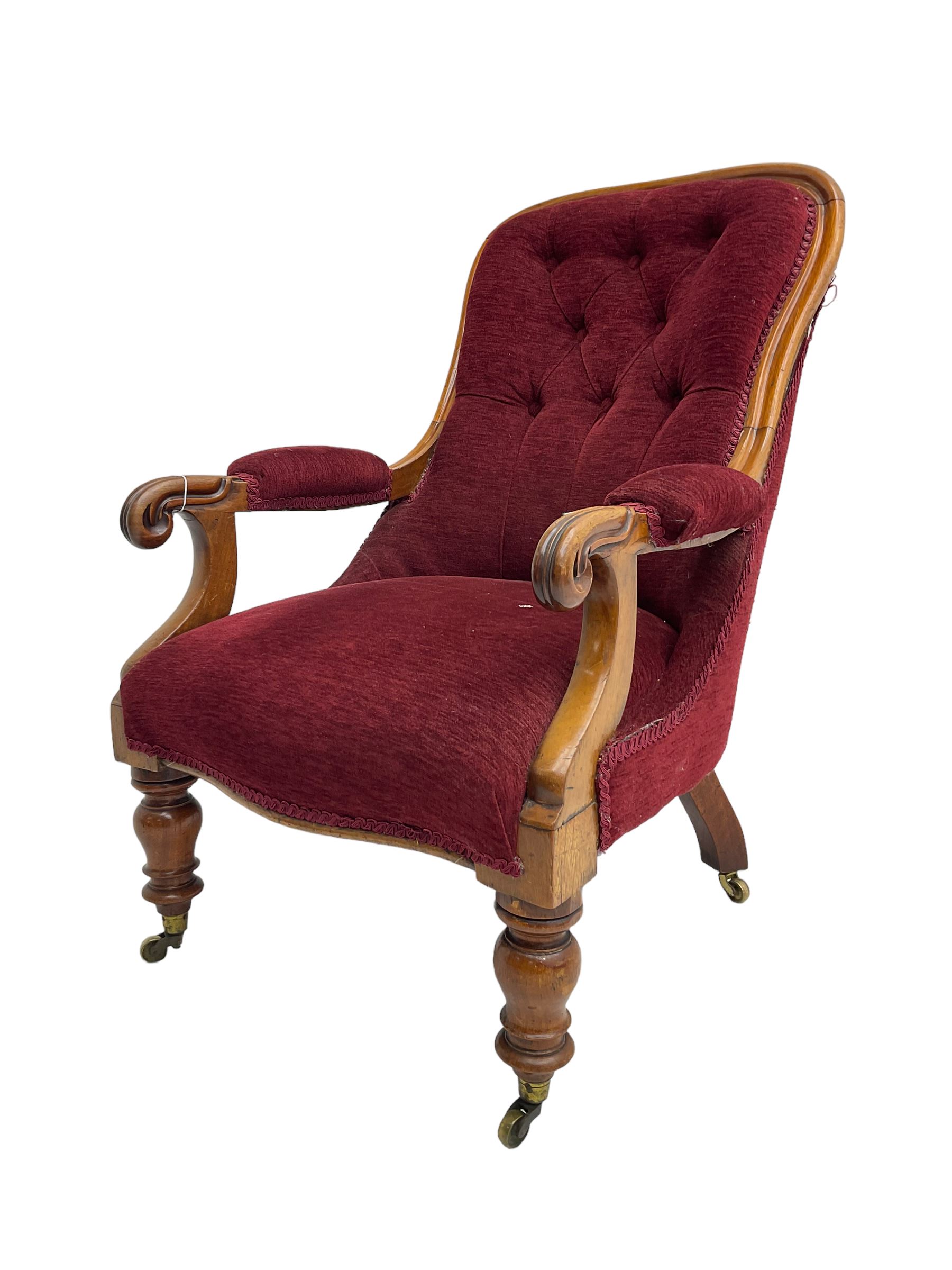 Victorian mahogany framed open armchair, upholstered in buttoned red fabric, the arm terminals carved with scrolls, on turned front supports with brass cups and castors