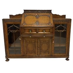 Early 20th century heavily carved oak bookcase bureau, raised back with grape-vine carved frieze, over fall-front enclosing fitted interior, above two short drawers and curved frieze drawer, flanked by astragal glazed and panelled cupboards, on turned feet