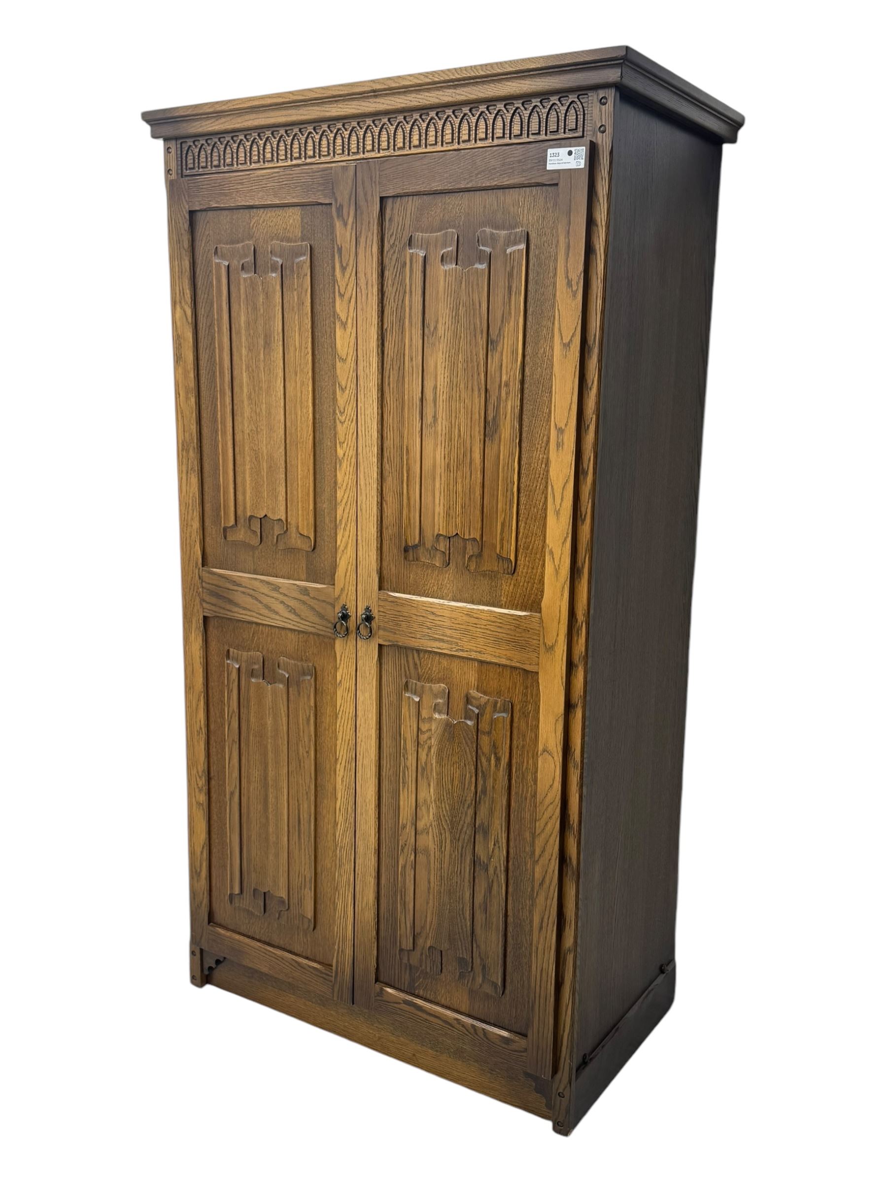 Jacobean design oak double wardrobe, projecting cornice over Gothic arched tracery carved frieze, twin panelled doors with linenfold relief carved detailing, on plinth base