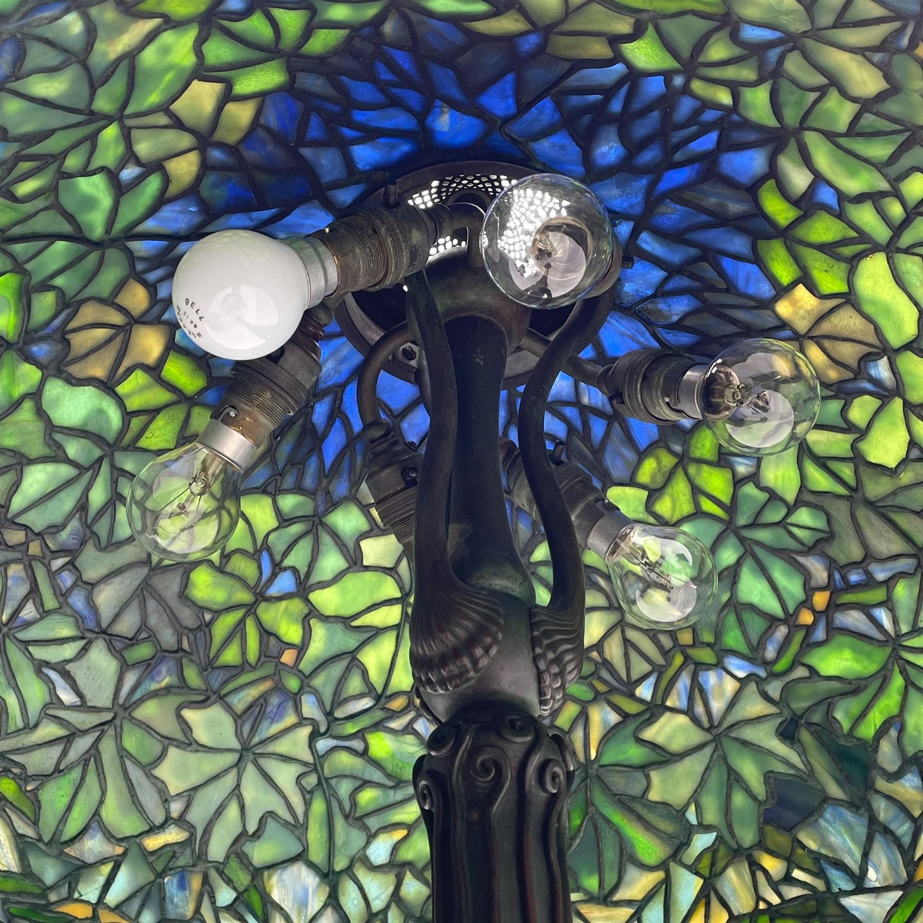 In the manner of Tiffany & Co. - bronze 'Chased Pod' design floor lamp, 'Maple Leaf' dome leaded glass shade decorated with flowers in blue and green shades, six branches on column decorated with stylised trailing stems terminating to circular base with stylised plant decoration, on scrolled feet, the base stamped 'Tiffany Studios New York 379' the inner shade stamped 'Tiffany Studios New York [...]'