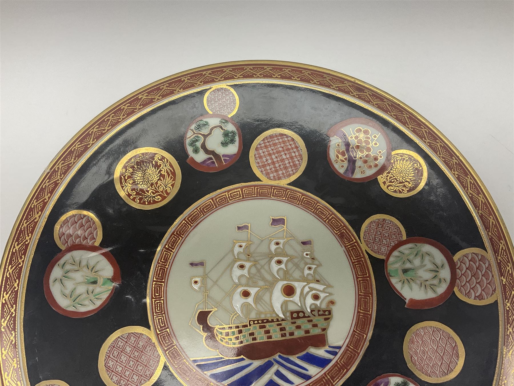 Chinese export charger, the centre decorated in enamel with a ship at full sail, surrounded by enamel panels of bamboo and cherry blossom with gilt edging on a black ground, with red and gilt border, with painted character marks beneath D34.4cm