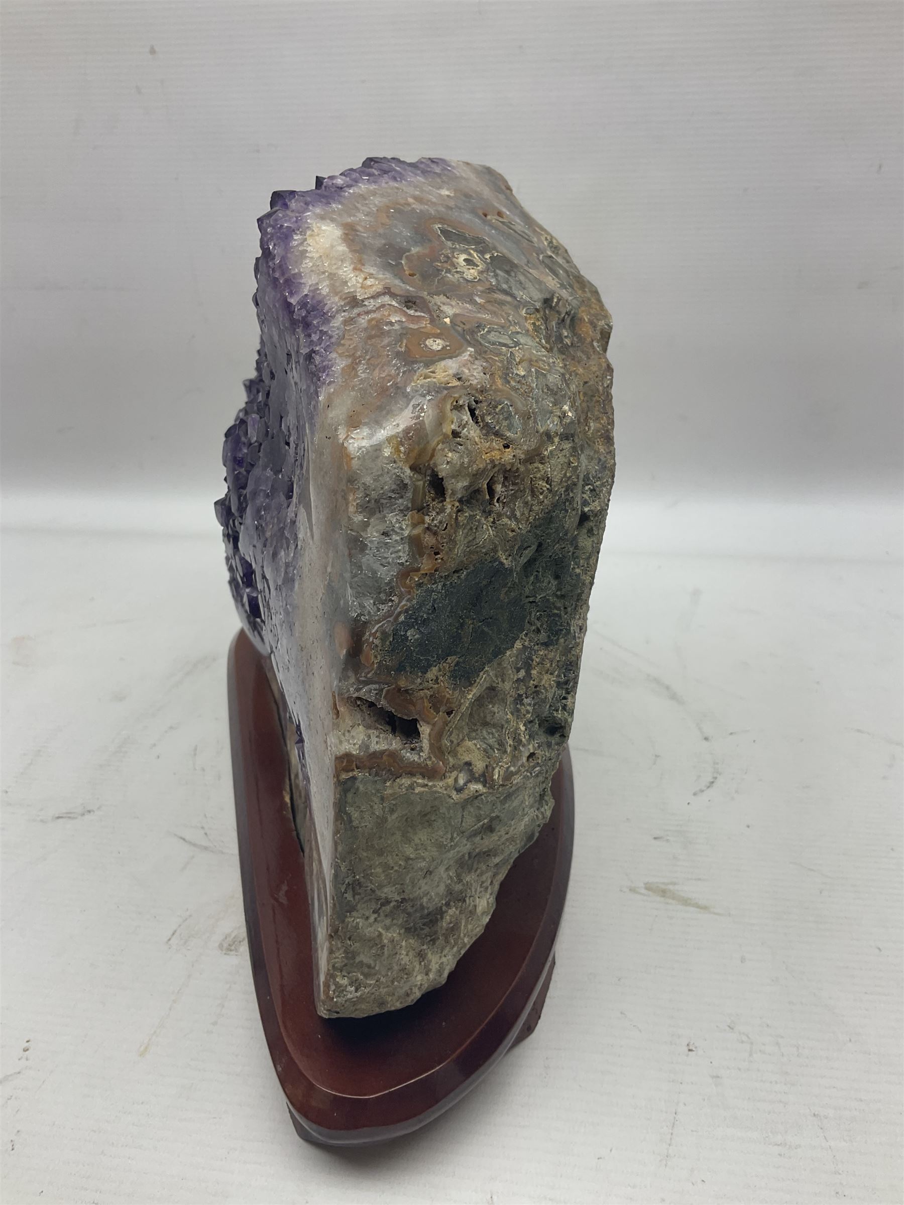 large amethyst crystal geode cluster, with well-defined crystals of various sizes, upon a carved wooden stand 