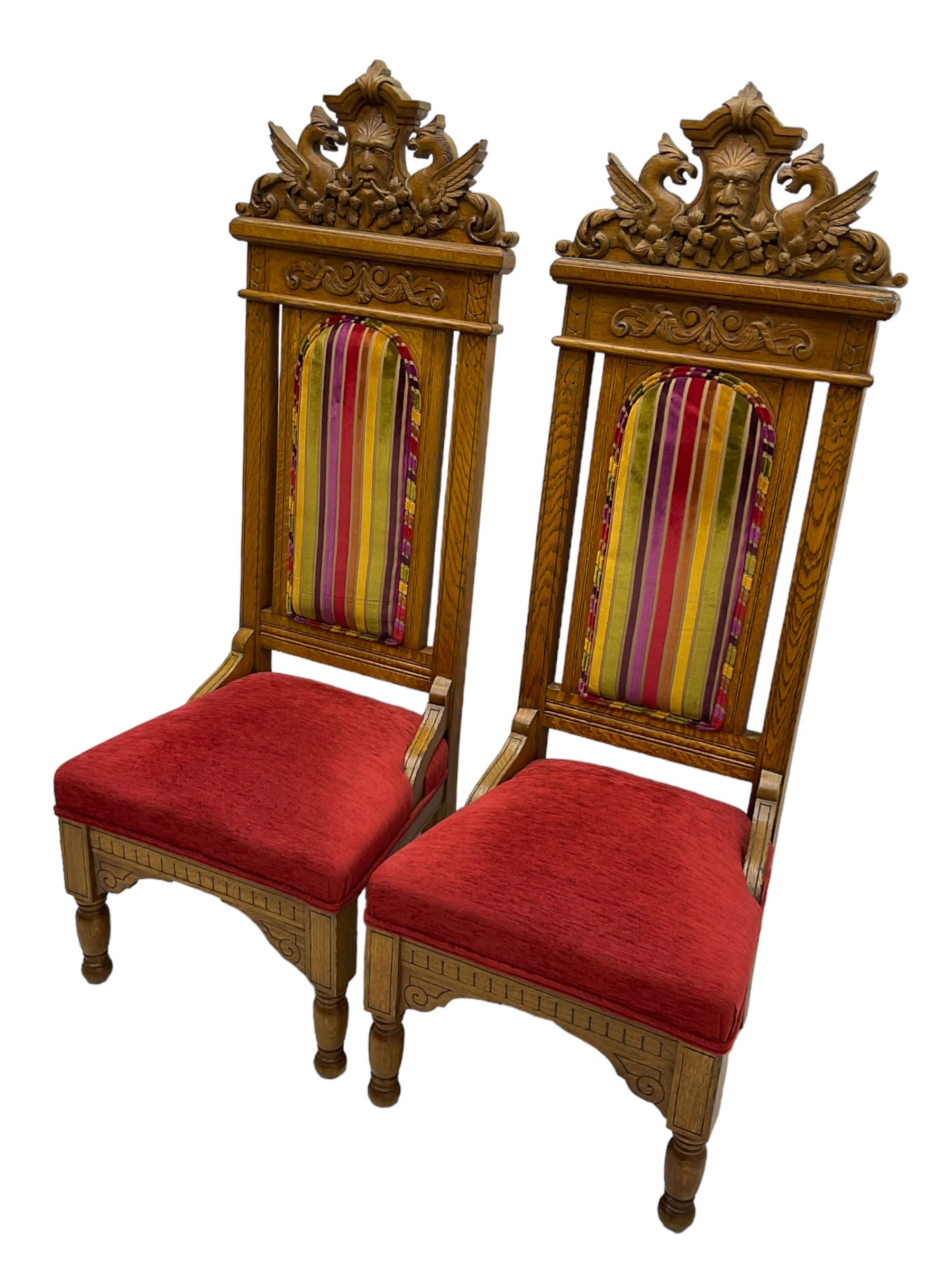 Set of six 20th century Carolean design oak high back chairs, the pediment carved with dragons and central Green Man mask with trailing foliage, the backs upholstered in striped fabric, on turned front supports