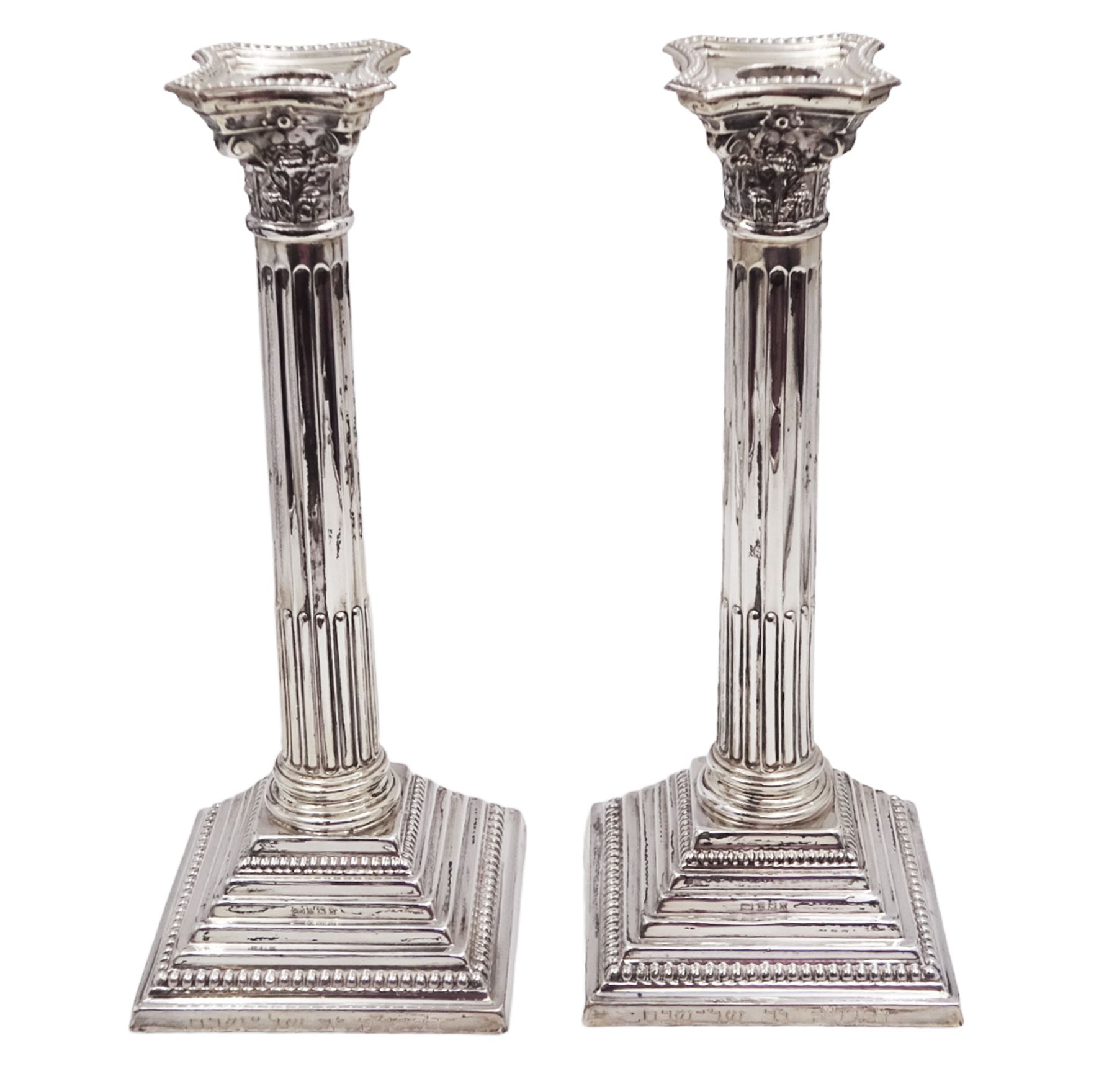 Pair of modern silver Corinthian column candlesticks, each with removable sconces with dart edging and embossed detailing, with personal engraving in a Semitic language, upon weighted stepped square bases, hallmarked Birmingham 1962, maker's marks HYC, H30.5cm