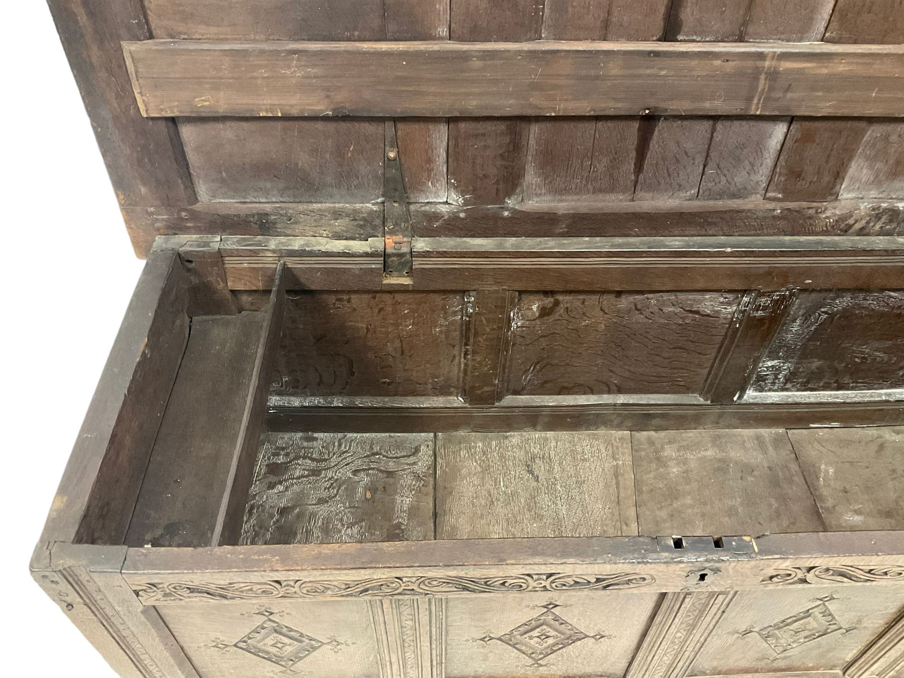 18th century oak coffer or chest, rectangular hinged panelled top with moulded frame enclosing candle box, the frieze carved with foliate S-scrolls over a quadruple panel front decorated with carved lozenges, on stile supports