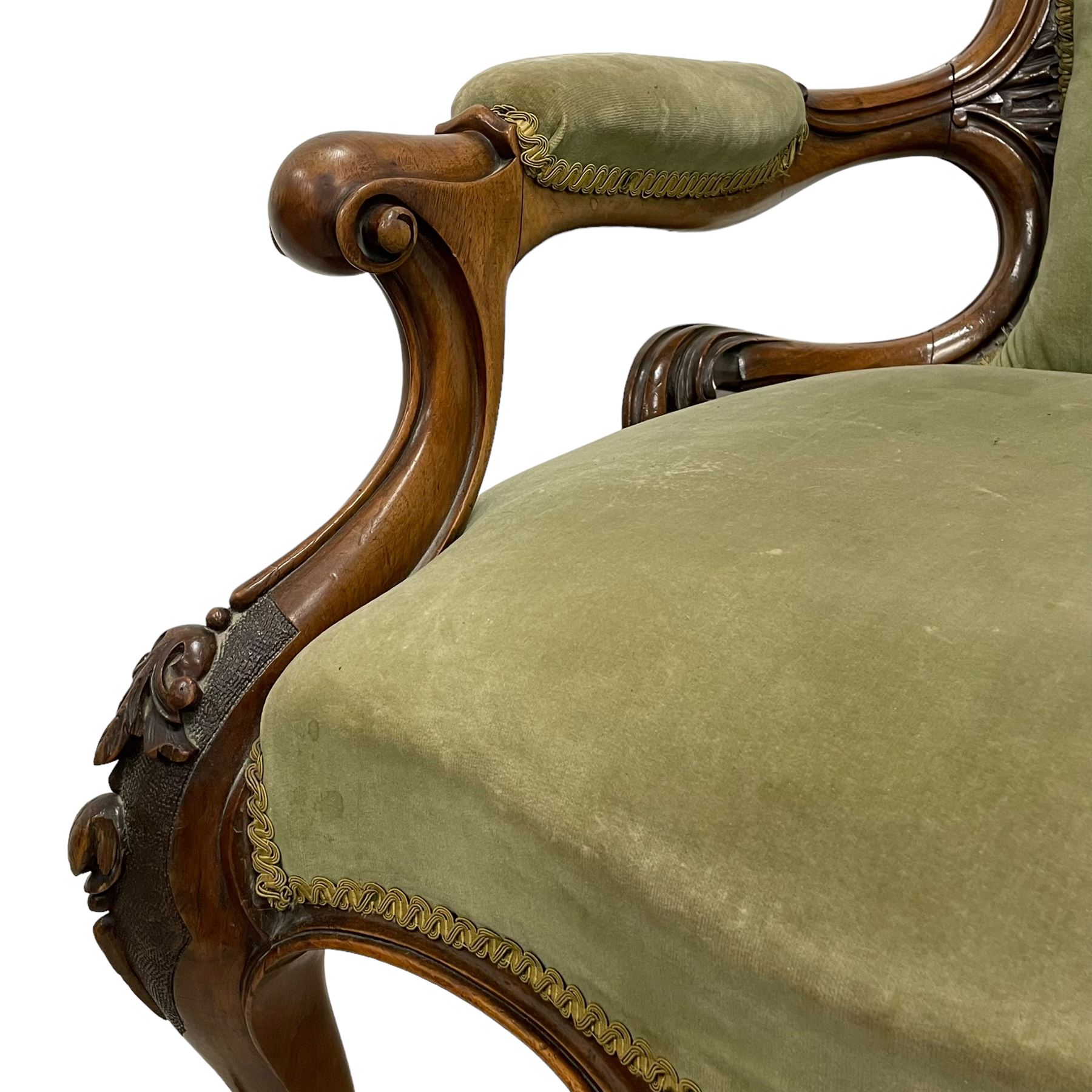 Pair of lady's and gentleman's Victorian carved walnut armchair and nursing chair, foliate carved cresting rail over shaped back with scrolled acanthus carved sides, the armchair with scroll arm terminals, the spoon back and sprung seat upholstered in buttoned sage green velvet, raised on cabriole supports with bell-flower moulded knees and scroll feet, on ceramic castors