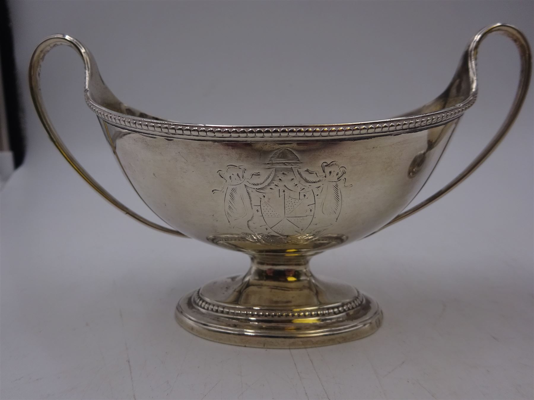 Pair of George III twin handled silver salts, of navette form with beaded rim and twin whiplash handles, each engraved to body with crest, upon stepped oval foot, London 1784, H8.5cm