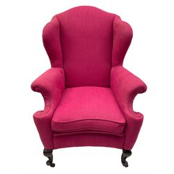 Georgian design hardwood-framed wingback armchair, arched cresting rail over curved wingback, rolled arms on scrolled cushioned supports, reverse bow-front, upholstered in claret red fabric with loose seat cushion, on cabriole front feet and brass castors 