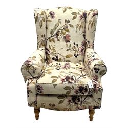 Hardwood-framed wingback armchair, upholstered in cream floral pattern fabric, on turned front feet