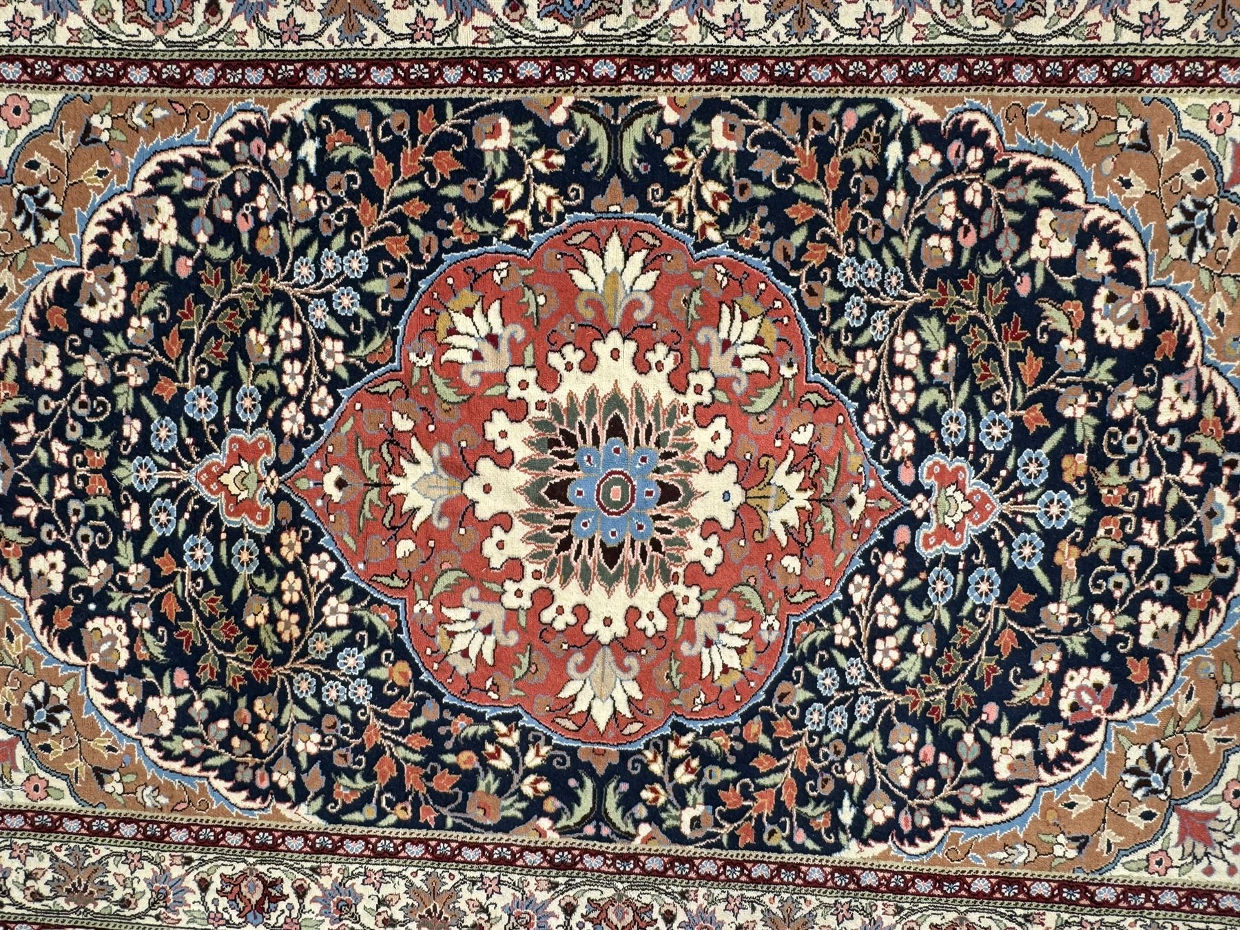 Indo-Persian indigo ground rug, the floral design peach medallion surrounded by trailing and interlaced branches and flower heads, the main border decorated with repeating stylised plant motifs within floral guard stripes 