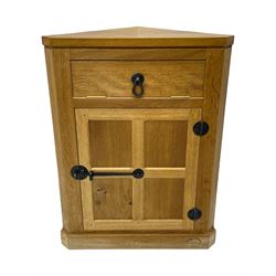 Mouseman - oak floor standing corner cupboard, fall front compartment over single panelled door, with wrought metal loop handle and latch, on moulded plinth base, carved in relief with mouse signature, by the workshop of Robert Thompson, Kilburn 