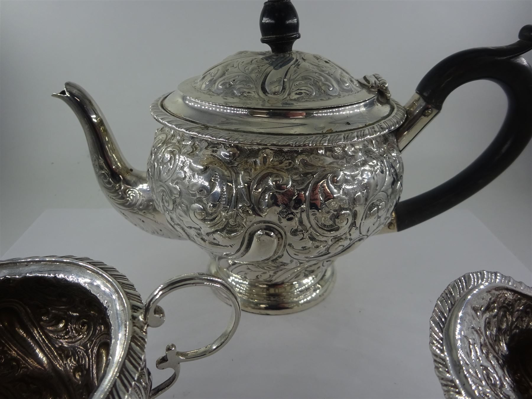 Late Victorian silver three piece bachelors tea service, comprising teapot, open sucrier and milk jug, each of bellied form, upon a circular stepped foot, and profusely embossed with foliate and scrolling decoration, the teapot with ebonised handle and finial, hallmarked George Nathan & Ridley Hayes, Birmingham 1894, teapot H14.5cm