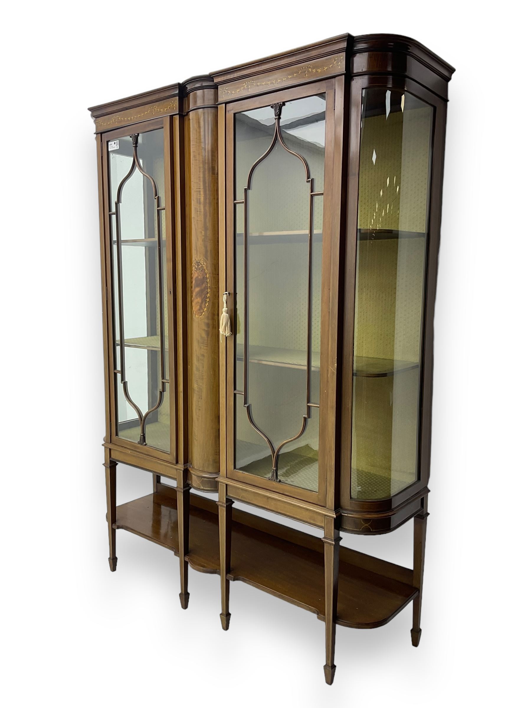 Edwardian inlaid mahogany display cabinet, projecting moulded cornice over two glazed doors, flanked by curved glazed sides and central arched panel with floral medallion, raised on square tapering supports with spade feet united by undertier