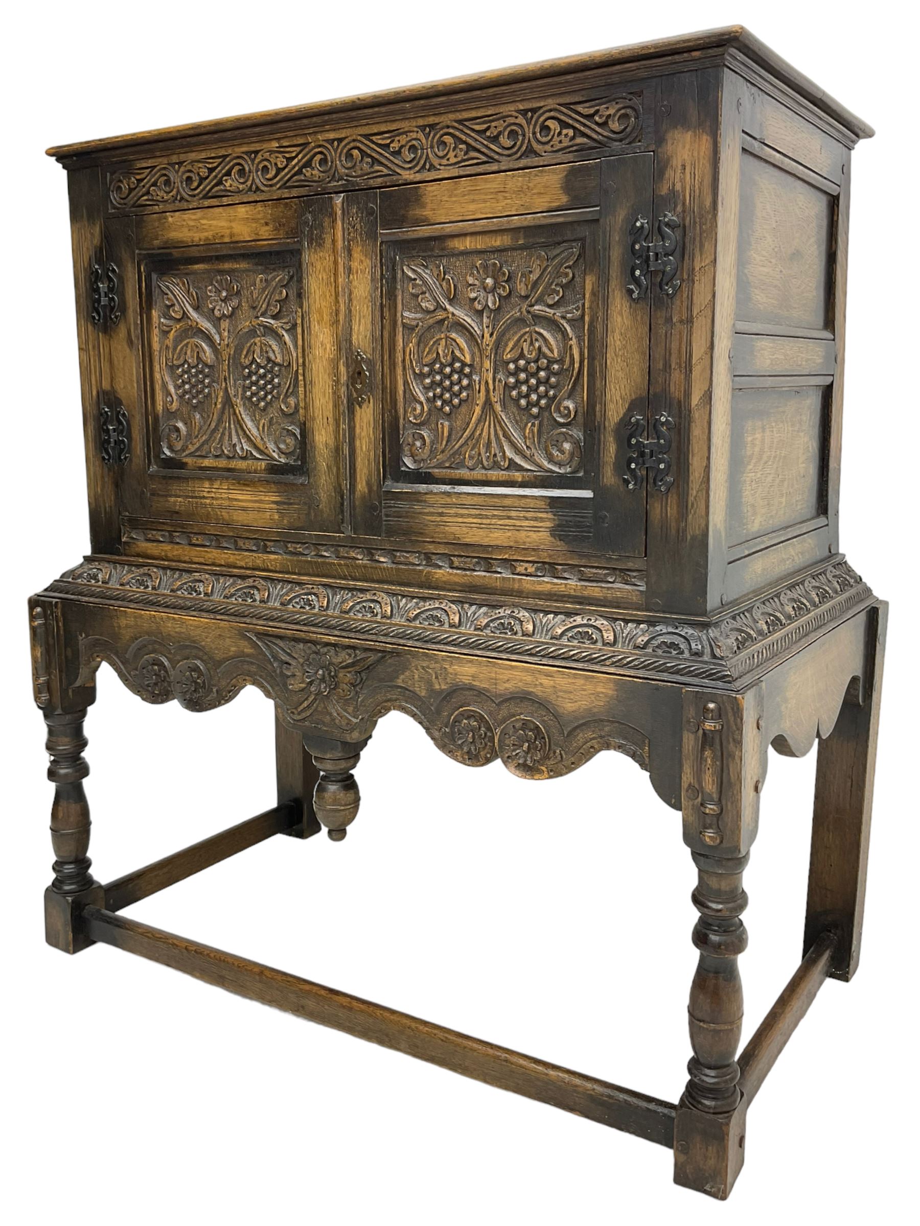 Jacobean Revival carved oak cupboard, moulded rectangular top over S-scroll carved frieze and two doors, the panelled doors carved with stylised plant motifs, on stand decorated with lunettes and shaped apron with hanging turned pendant, on turned supports united by stretchers 