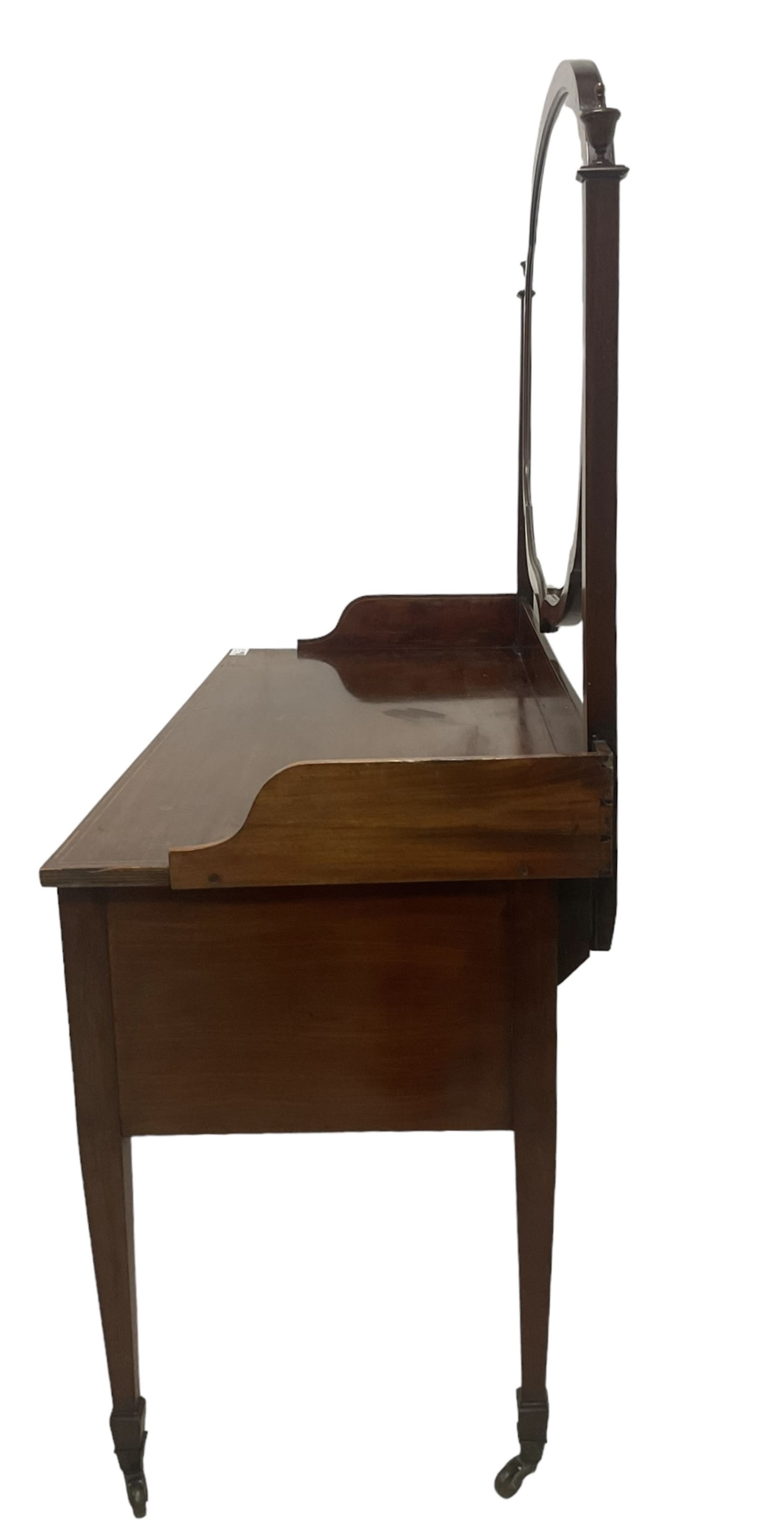 Edwardian inlaid mahogany kneehole dressing table, raised shaped oval bevelled mirror back, fitted with five drawers with banding and stringing, on square tapering supports with castors