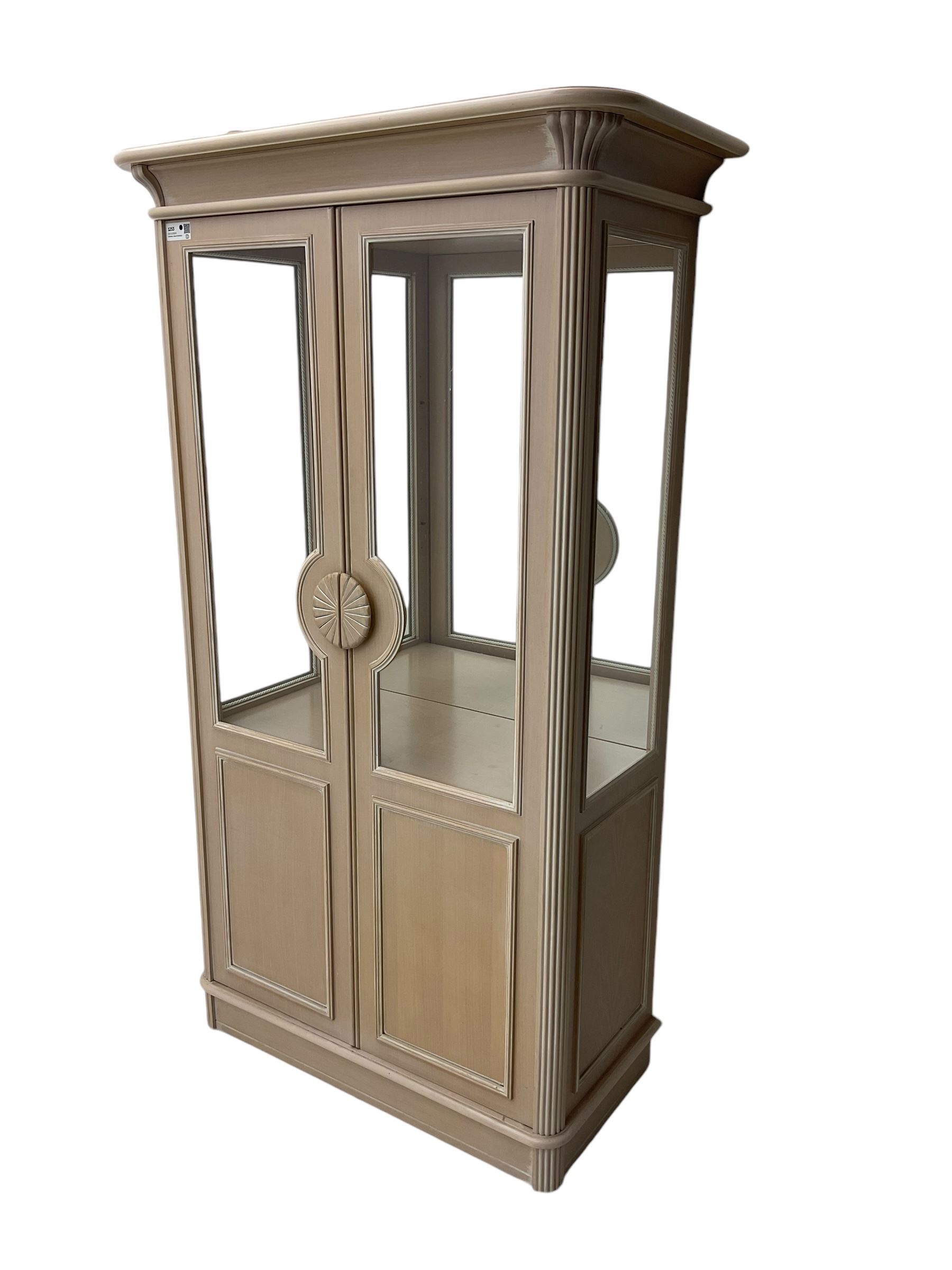 Contemporary display cabinet, moulded cornice above glazed panelled doors with central carved sunburst handles, mirrored back interior with lighting, lower enclosed storage compartment, raised on plinth base