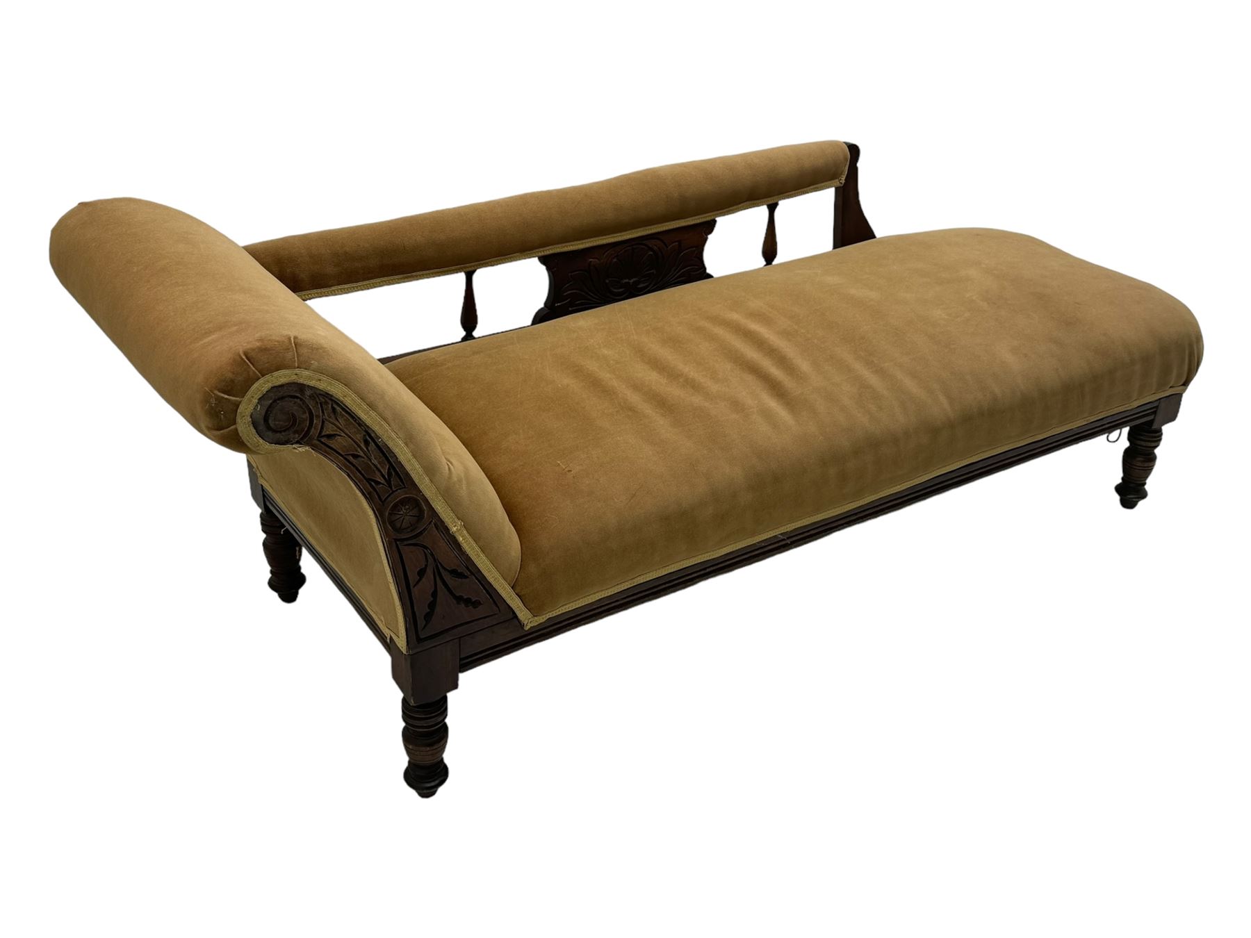 Late 19th century mahogany framed chaise longue, upholstered in tan fabric, featuring scrolled backrest with carved floral motifs, supported by turned legs