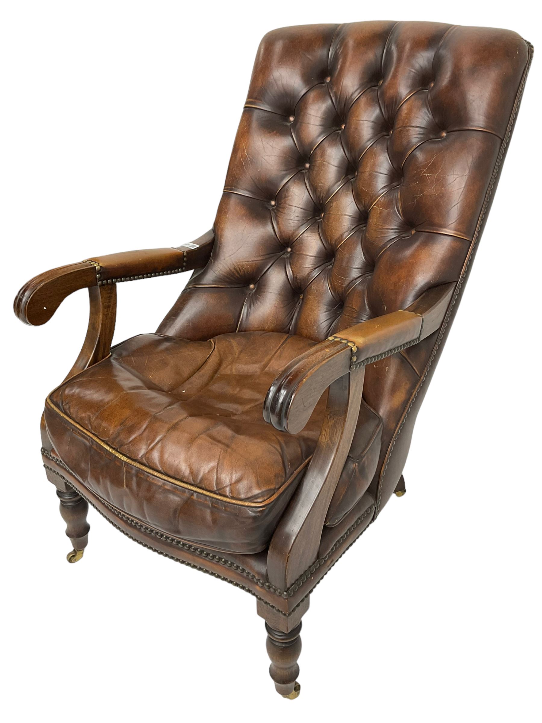 Georgian design mahogany framed library armchair, upholstered in buttoned chocolate brown leather with studwork and loose seat cushion, raised on turned supports with brass castors