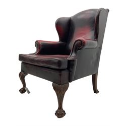 Georgian design hardwood-framed wingback armchair, upholstered in red leather, loose seat cushion and rolled arms, on acanthus carved ball and claw front feet 