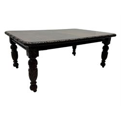 19th century heavily carved oak extending dining table, rectangular top with rounded corners and carved gadrooned edge, extending via winding mechanism with two additional leaves, raised on acanthus leaf-carved baluster supports terminating in ceramic castors