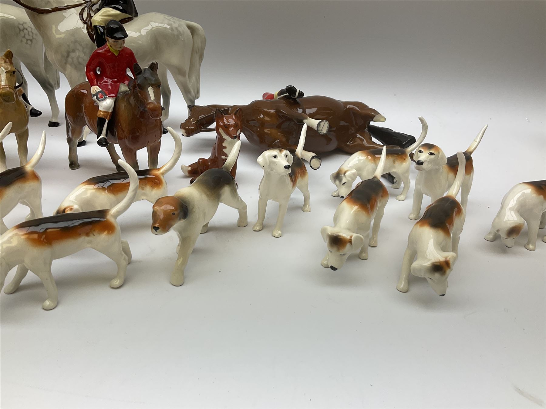 Beswick Hunting Group, comprising: two huntswoman on grey horses, model no 1730, huntsman on a bay horse, model no 1501, a seated fox, model no 1748, eighteen fox hounds and a spaniel, model no 967, all with printed marks beneath, together with three other ceramic huntsman on horseback and two hounds. 