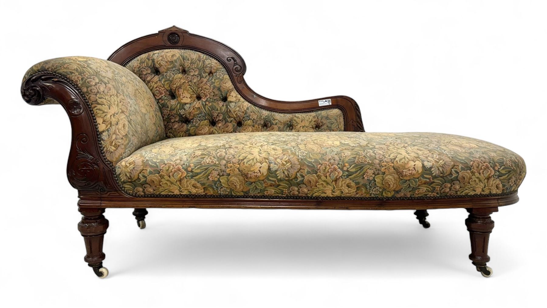 Victorian Aesthetic Movement mahogany framed chaise longue, shaped carved back over acanthus scrolled arm terminal, upholstered in floral patterned tapestry fabric with sprung seat, on turned and fluted supports with castors