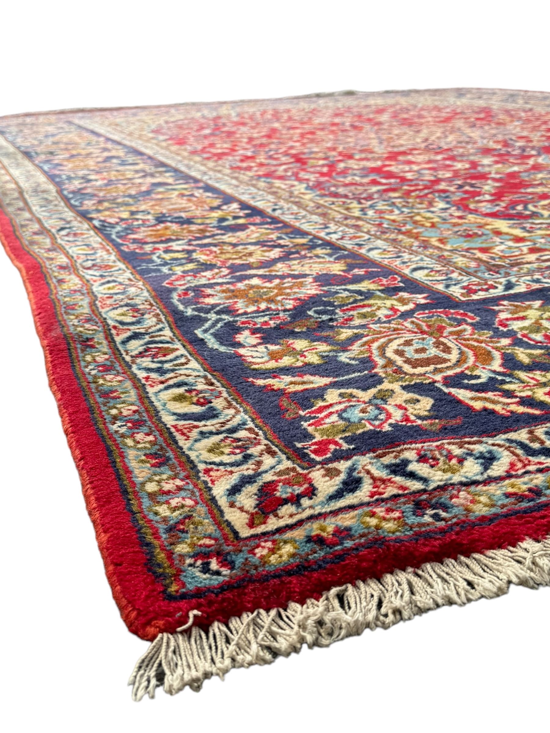 Persian Kashan red ground rug, the field decorated with a central floral medallion surrounded buy scrolling vine motifs and palmettes, the main border featuring a series of stylised floral motifs against a dark blue ground, enclosed by multiple guard stripes with alternating floral and geometric designs