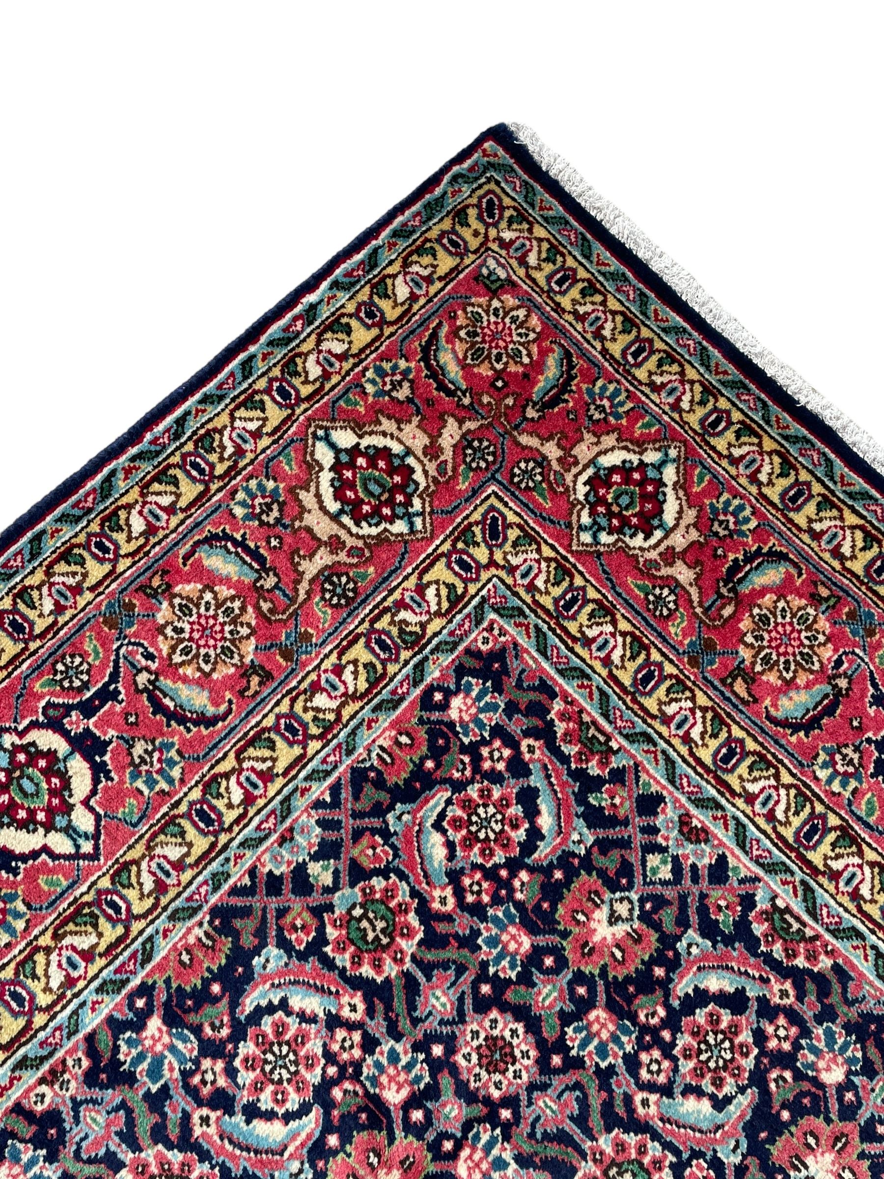 Persian Farahan indigo ground rug, the field decorated with large repeating floral herati motifs, crimson ground border decorated with palmettes and trailing leafy branch, within guard stripes 