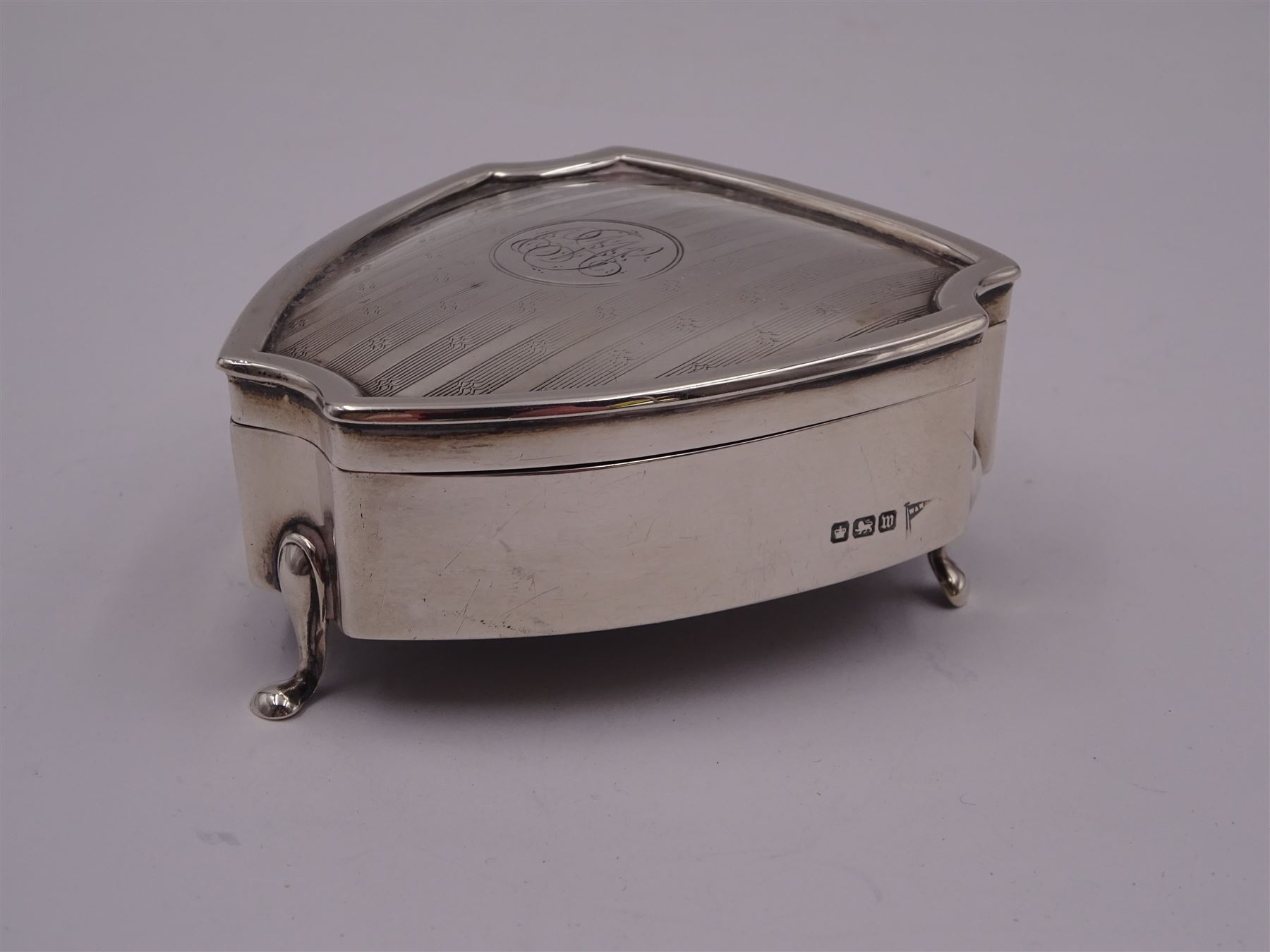 Early 20th century silver mounted trinket box, of shield form, with engine turned decoration and engraved circular cartouche to hinged cover, opening to reveal green velvet interior, upon three pad feet, hallmarked Walker & Hall, Sheffield 1914, H3.5cm, W7cm