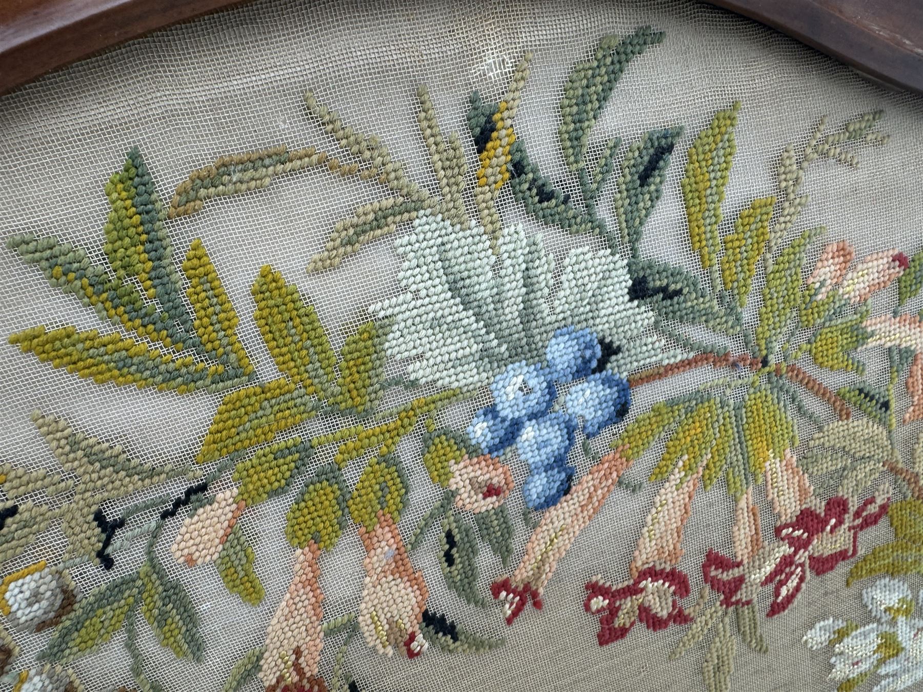 Early 20th century walnut carved needlepoint wall panel, depicting peacock amongst a floral arrangement, framed by carved border with scrolled crest and acanthus leaf accents