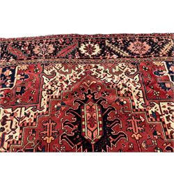 Persian Heriz red ground carpet, large central eight point medallion with projecting palmettes surrounded by small geometric motifs, decorated profusely with hooks, rosettes and animals, the busy border decorated with stylised foliate motifs within guard stripes 