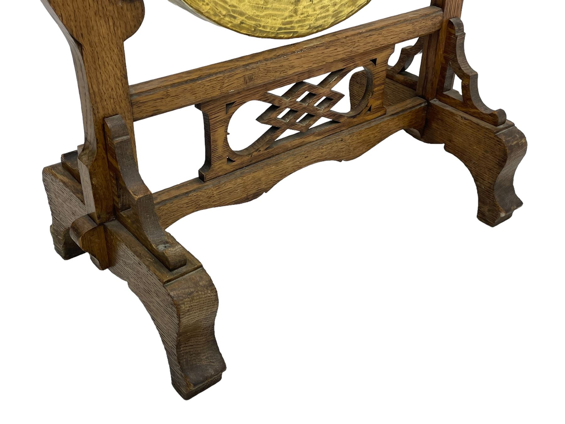 Early 20th century oak gong stand with gong and hammer, shaped cresting rail over moulded upper edge on shaped supports, hanging brass drum gong over fretwork middle rail, on raised platforms terminating to splayed feet