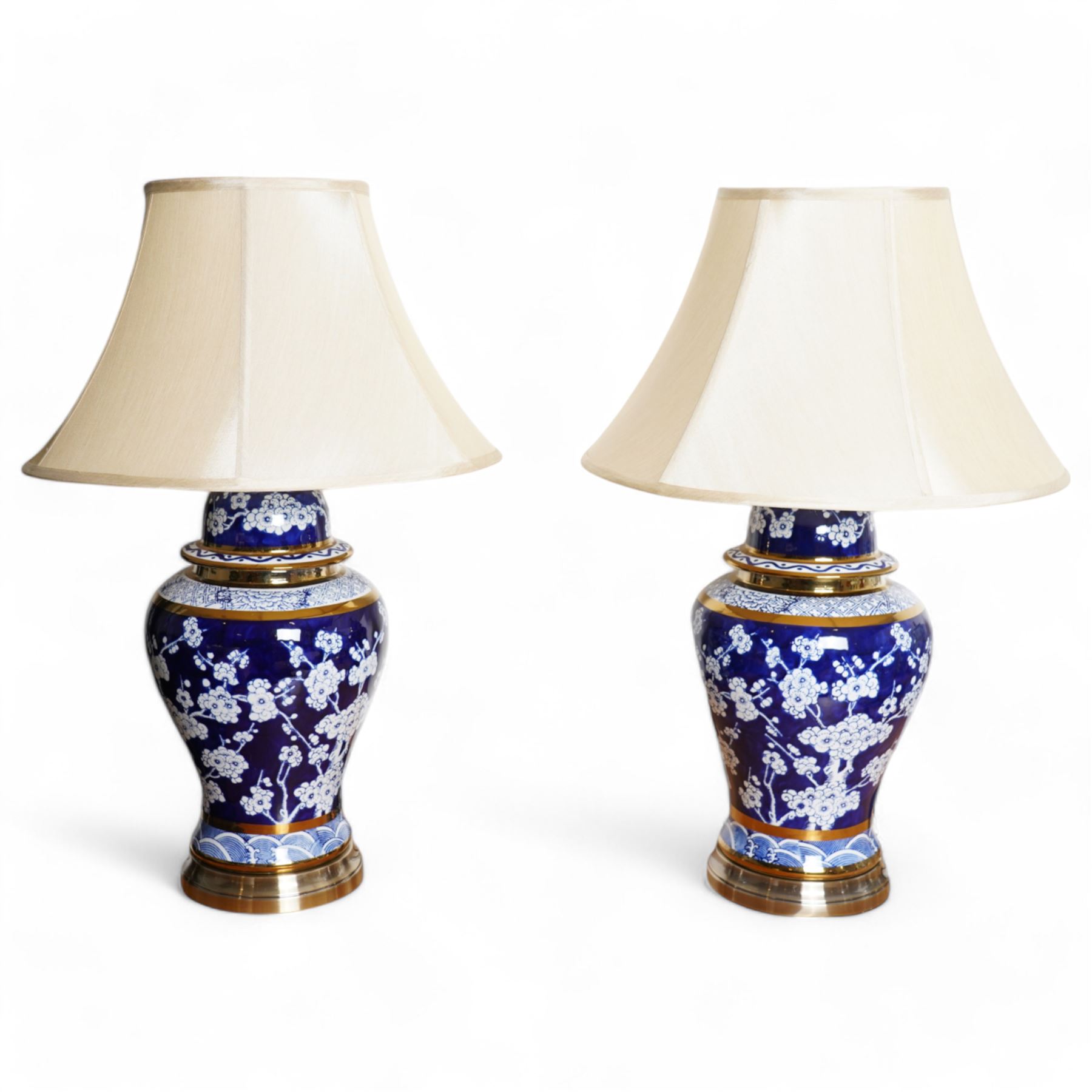 Pair of blue and white table lamps, each in the form of a vase and cover, decorated with cherry blossom, within foliate and geometric borders, raised upon circular gilt bases, H48cm including shades