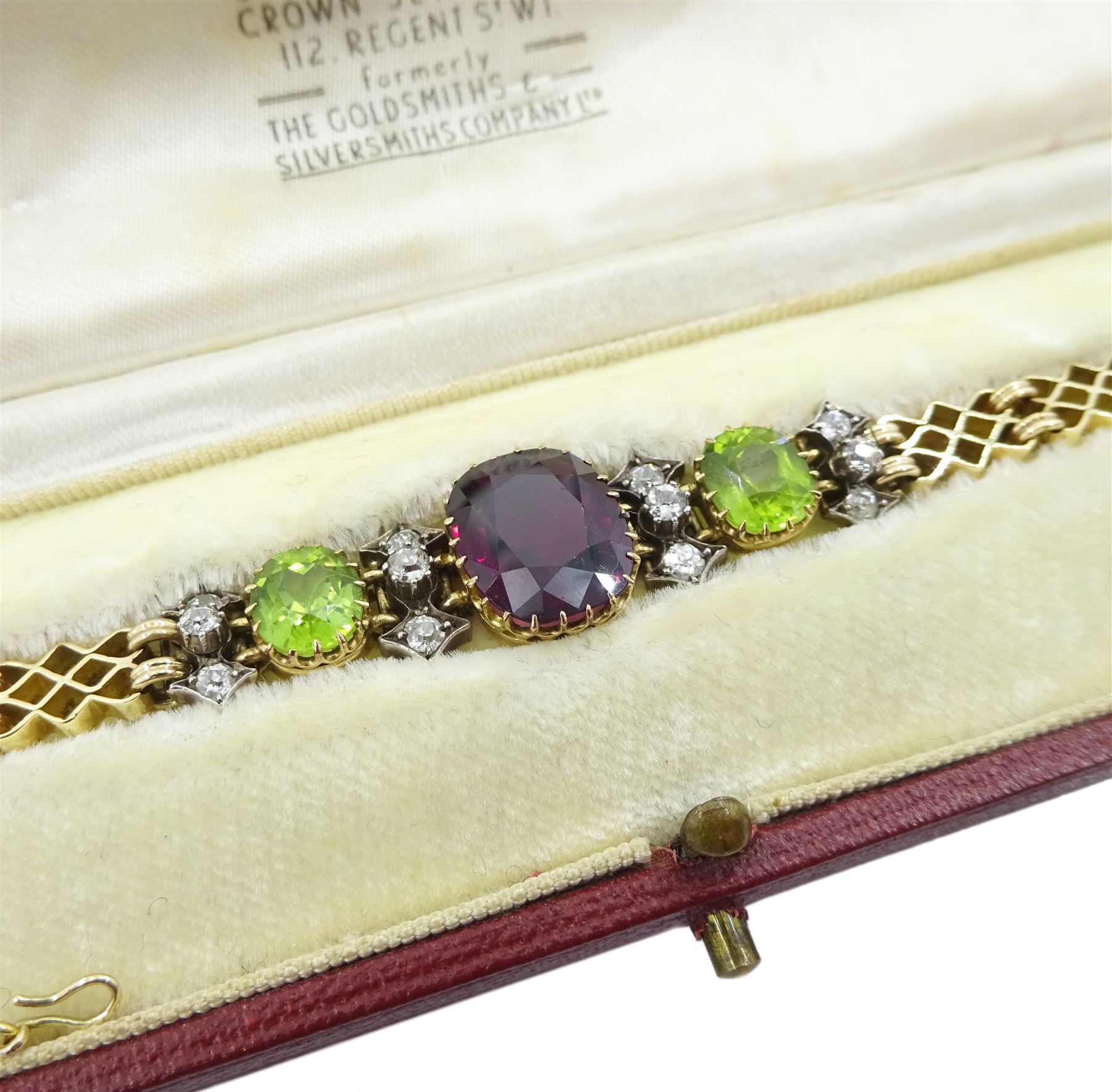 Early 20th century 15ct gold garnet, peridot and diamond, fancy link chain bracelet, the central cushion cut rhodolite garnet of approx 5.05 carat, with two cushion cut peridots set either side, spaced by three old cut diamonds, total diamond weight approx 0.35 carat, in fitted case by Garrard & Co