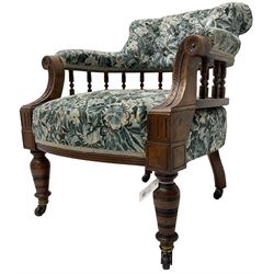 Victorian walnut framed tub-shaped armchair, the shaped rolled back supported by a spindle turned balustrade, upholstered in buttoned floral fabric, scrolled arms supports carved with acanthus leaves and flower heads, on collar turned feet with brass and ceramic castors