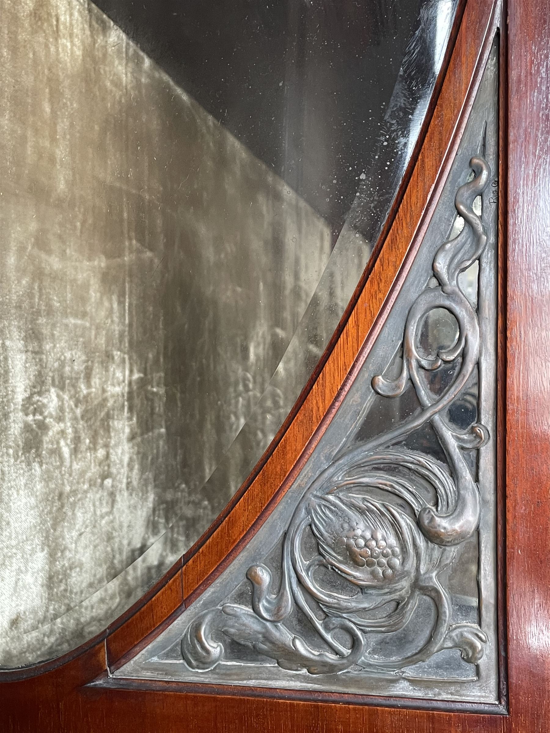 Art Nouveau period inlaid mahogany display cabinet, raised shaped and moulded pediment over projecting moulded cornices, the upper frieze inlaid with trailing branches and tulips, single astragal and bevel glazed door enclosed velvet lined interior fitted with shelves, flanked by curved glass panes decorated with pierced metal foliate spandrels, lower flanking shelves with mirror backs enclosed within shaped and pierced rails inlaid with flower heads, on tapering octagonal supports terminating to compressed pad feet, the lock stamped 'Salmon Bros, London' 