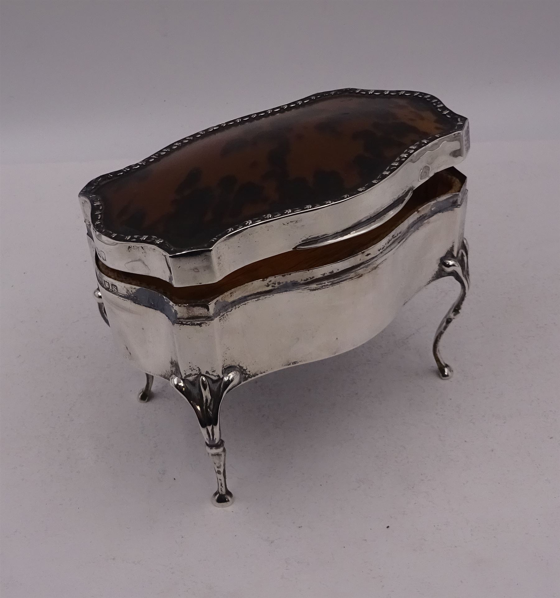 Early 20th century silver mounted jewellery casket, the slightly domed hinged cover set with a tortoiseshell panel, with a embossed floral border, opening to reveal a pleated silk lined interior, upon four cabriole legs, hallmarked Charles Boyton & Son Ltd, London 1913, H10cm