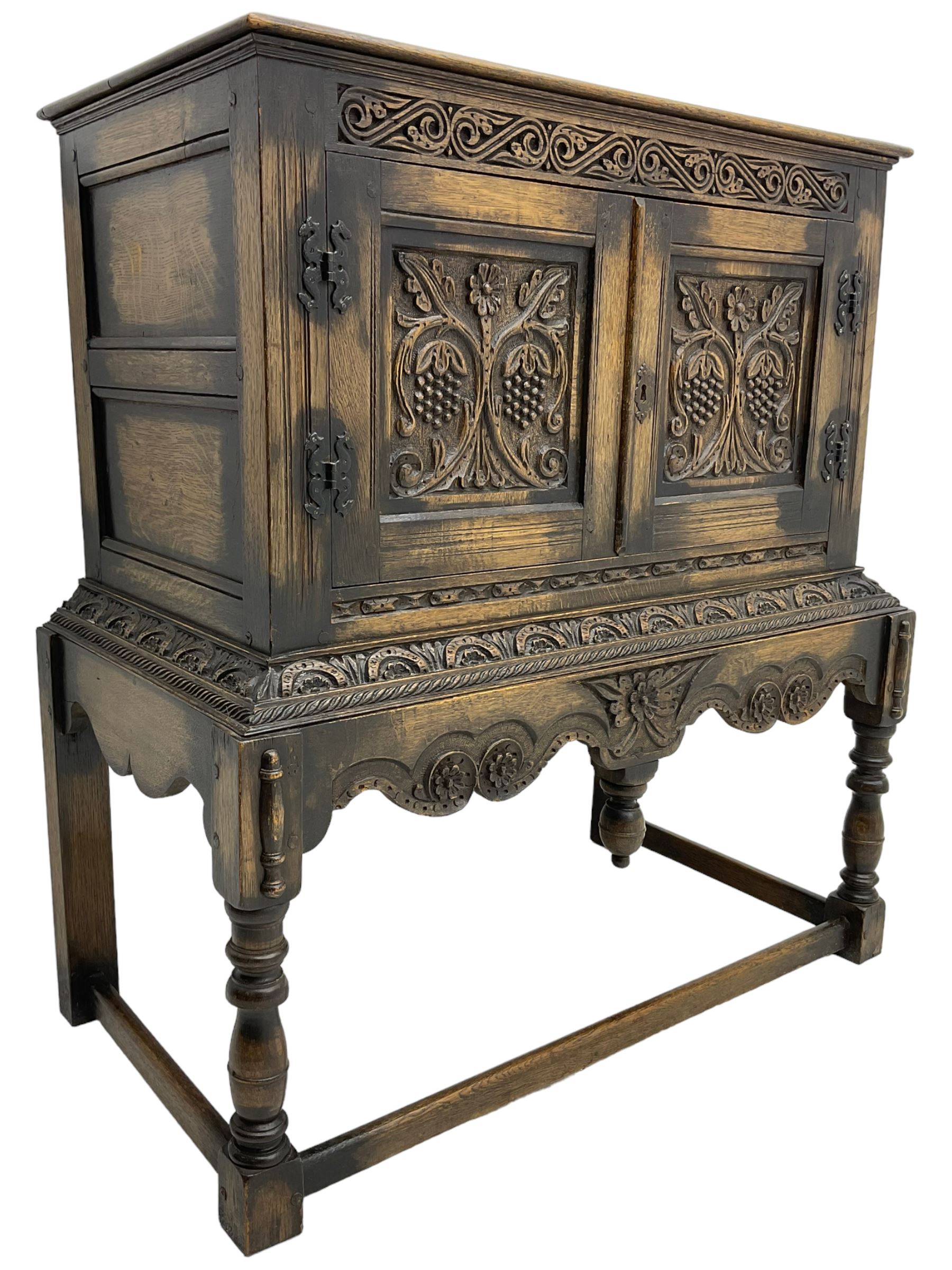 Jacobean Revival carved oak cupboard, moulded rectangular top over S-scroll carved frieze and two doors, the panelled doors carved with stylised plant motifs, on stand decorated with lunettes and shaped apron with hanging turned pendant, on turned supports united by stretchers 