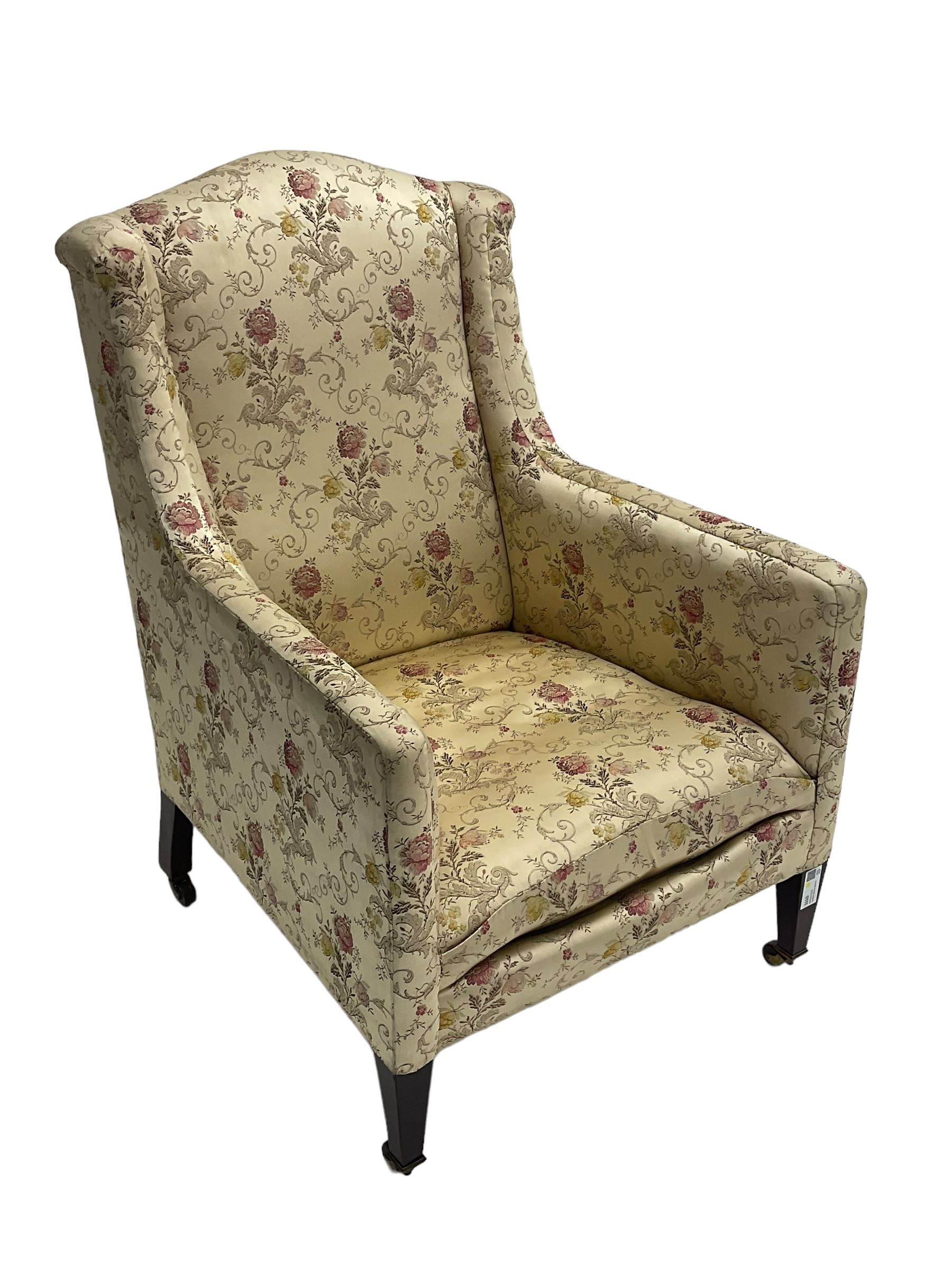 Edwardian hardwood-framed armchair, upholstered in floral pattern fabric, on square tapering front supports, brass and ceramic castors 