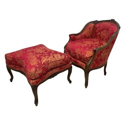 Late 20th century French design stained beech framed armchair and matching stool - the armchair with shaped and moulded frame carved with flower heads and foliage, upholstered in silk red and gold ground fabric with floral pattern, on scroll carved cabriole feet decorated with flower head carvings (W73cm, H82cm, D75cm); the footstool of concaved rectangular form with moulded frame carved with flower heads, upholstered loose cushion, on cabriole feet (70cm x 64cm, H48cm)