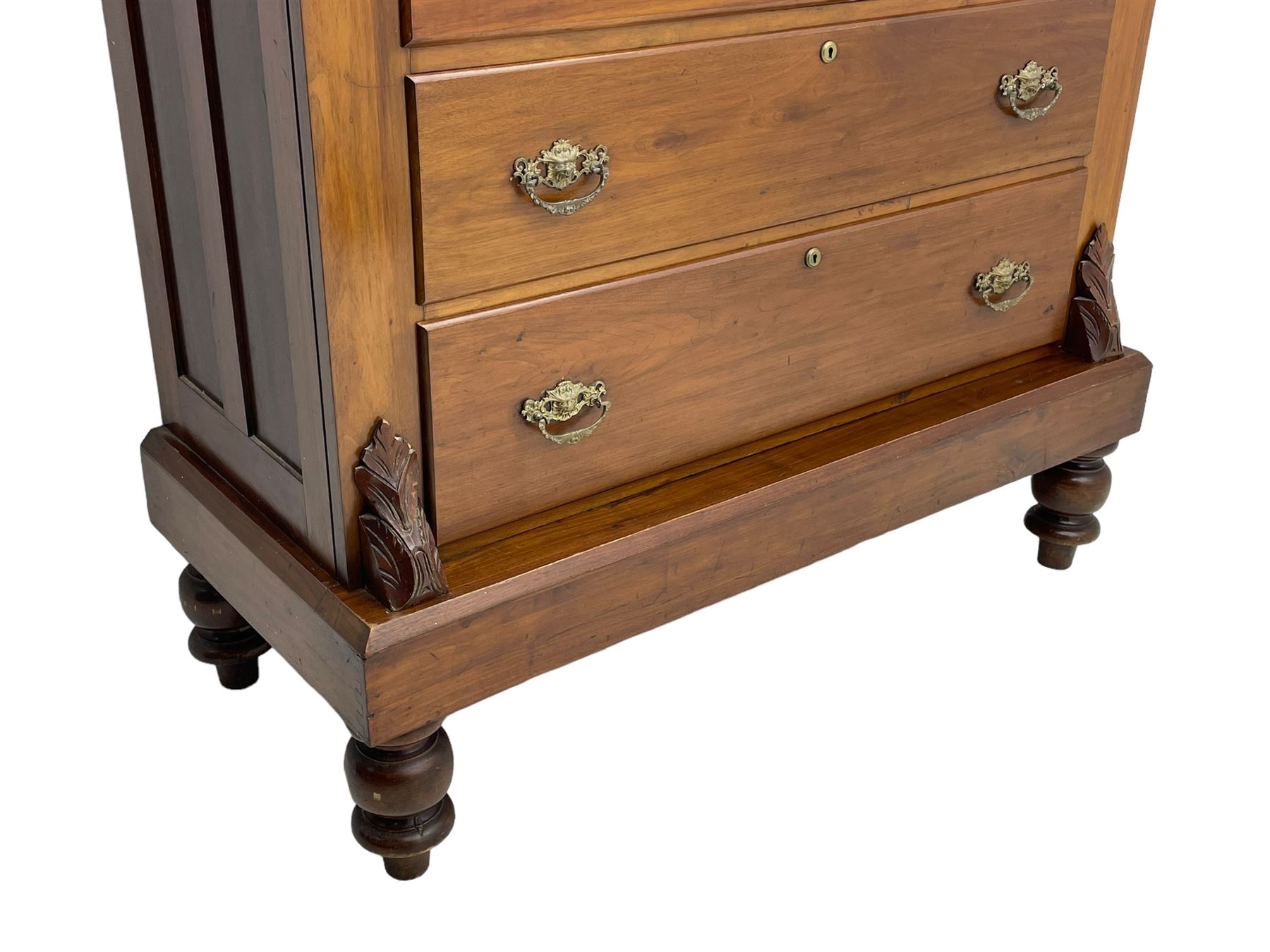 Late Victorian walnut Scotch chest, projecting cornice with turned quarter column mounts over matching half column to frieze, fitted with two upper short drawers with central cupboard, bevelled mirror glazed cupboard door, four graduating drawers below, foliage and flower head carved brackets to the uprights, panelled sides, chamfered plinth on turned feet