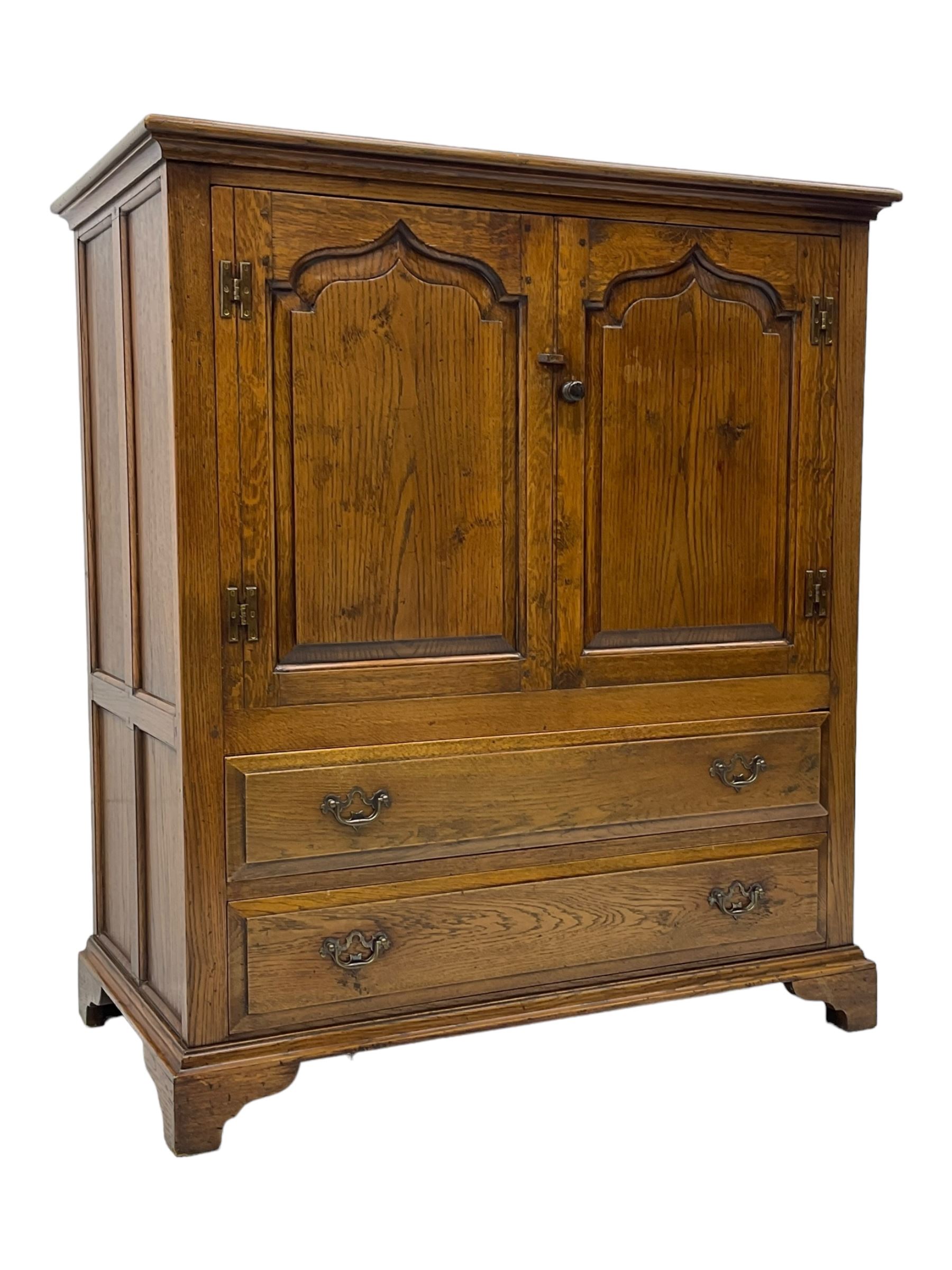 Oak drinks or media cabinet, projecting moulded cornice over two Gothic arch panelled doors on sliding tracks enclosing open storage, two drawers with brass drop handles, on bracket supports