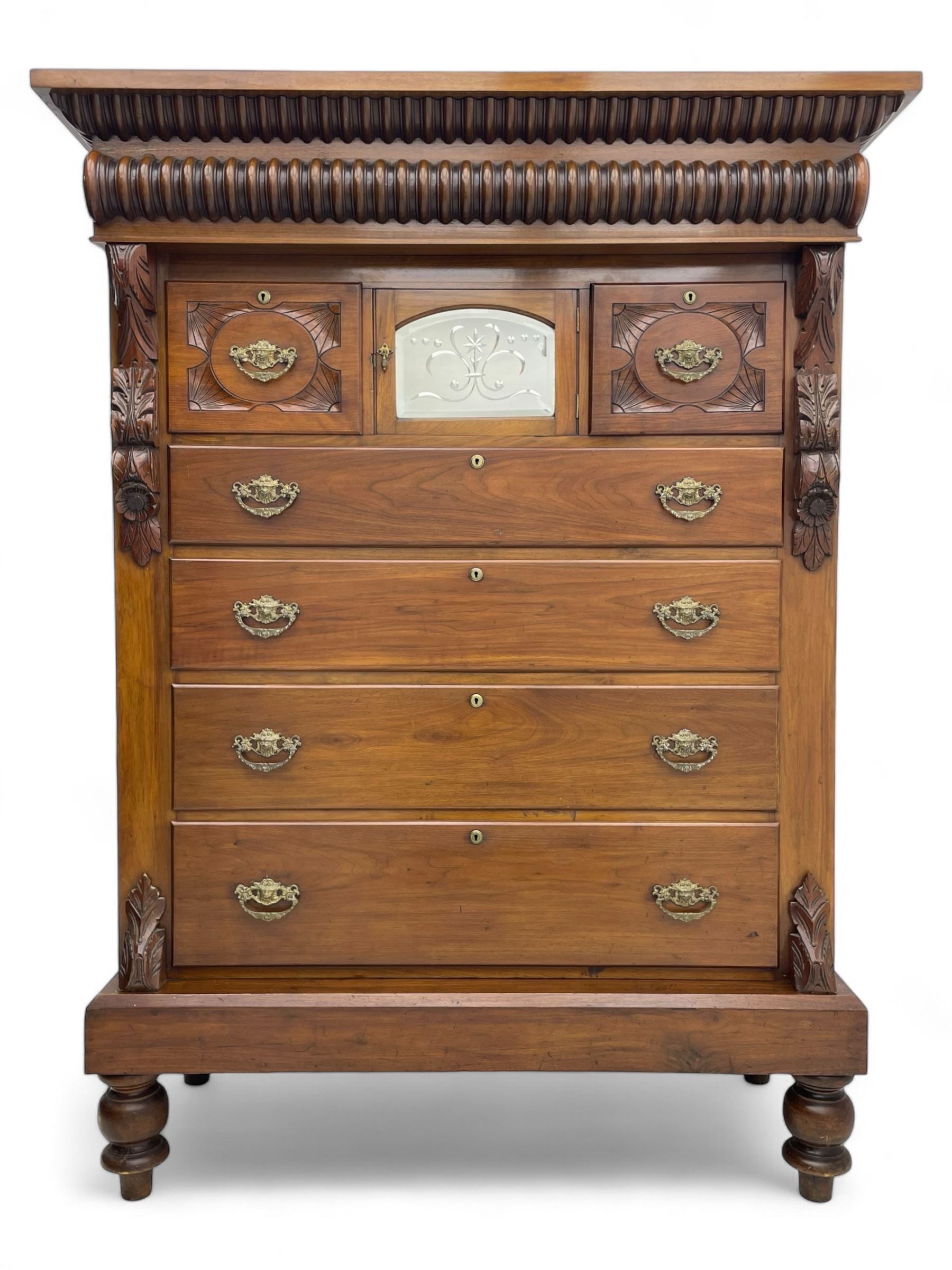 Late Victorian walnut Scotch chest, projecting cornice with turned quarter column mounts over matching half column to frieze, fitted with two upper short drawers with central cupboard, bevelled mirror glazed cupboard door, four graduating drawers below, foliage and flower head carved brackets to the uprights, panelled sides, chamfered plinth on turned feet