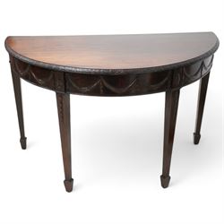 Early 20th century Hepplewhite Revival mahogany console table, demi-lune top with carved moulded edge, the frieze decorated with moulded repeating festoons, raised on square tapering supports with applied bell-flower motifs, terminating in spade feet