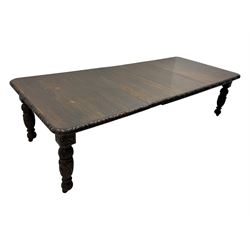 19th century heavily carved oak extending dining table, rectangular top with rounded corners and carved gadrooned edge, extending via winding mechanism with two additional leaves, raised on acanthus leaf-carved baluster supports terminating in ceramic castors