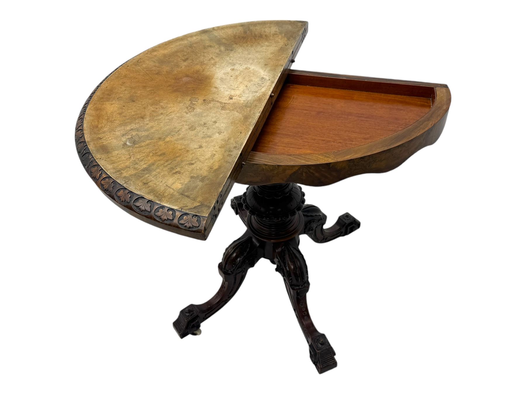 Victorian walnut demi-lune card table, circular fold-over top with foliate carved edge, revealing green baize-lined playing surface over scalloped apron, raised on a turned and carved pedestal with four splayed scroll supports with castors