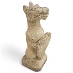 Near pair of cast stone garden seated dragons, snarling jaw holding shield on chamfered base 