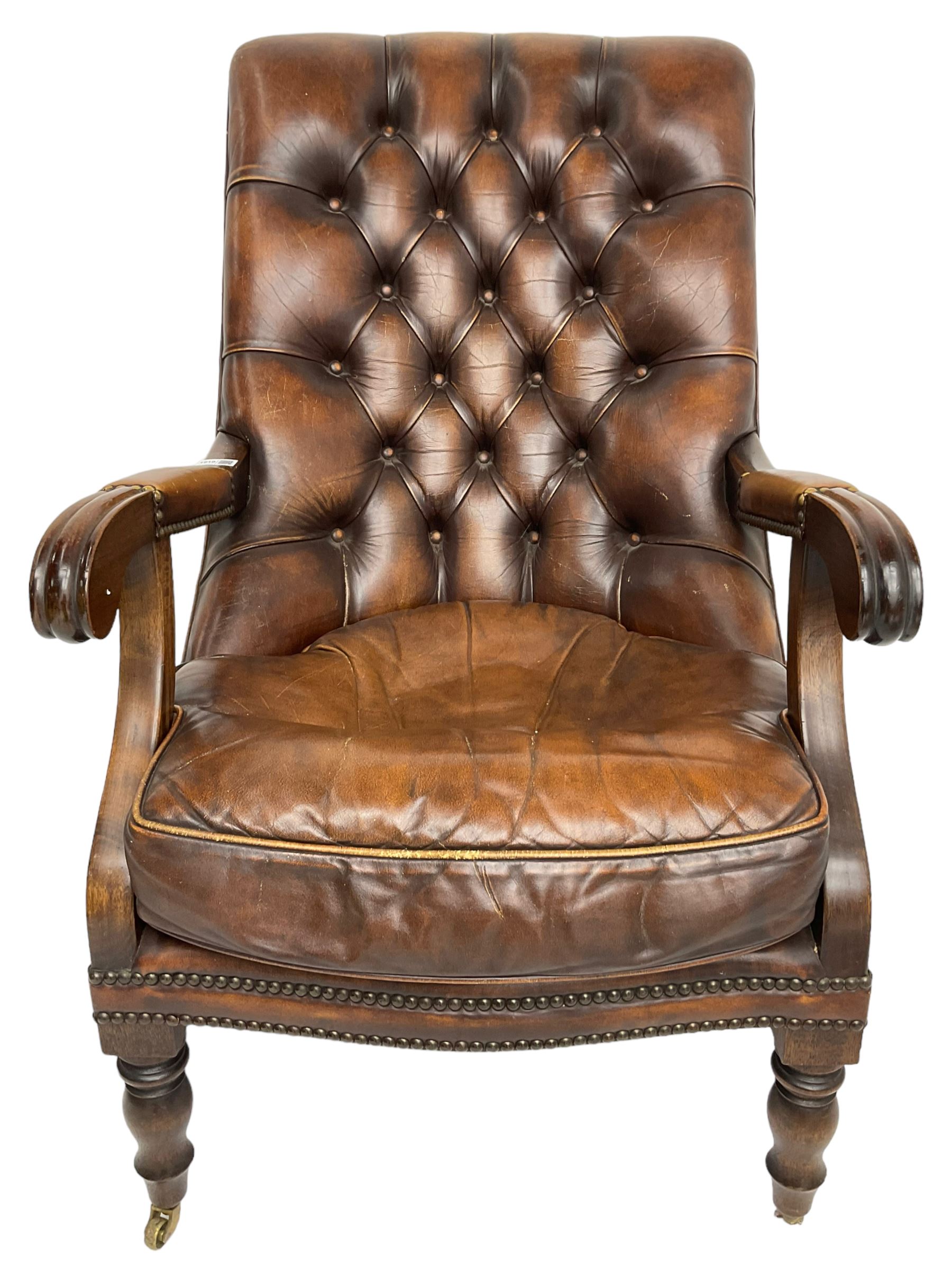 Georgian design mahogany framed library armchair, upholstered in buttoned chocolate brown leather with studwork and loose seat cushion, raised on turned supports with brass castors