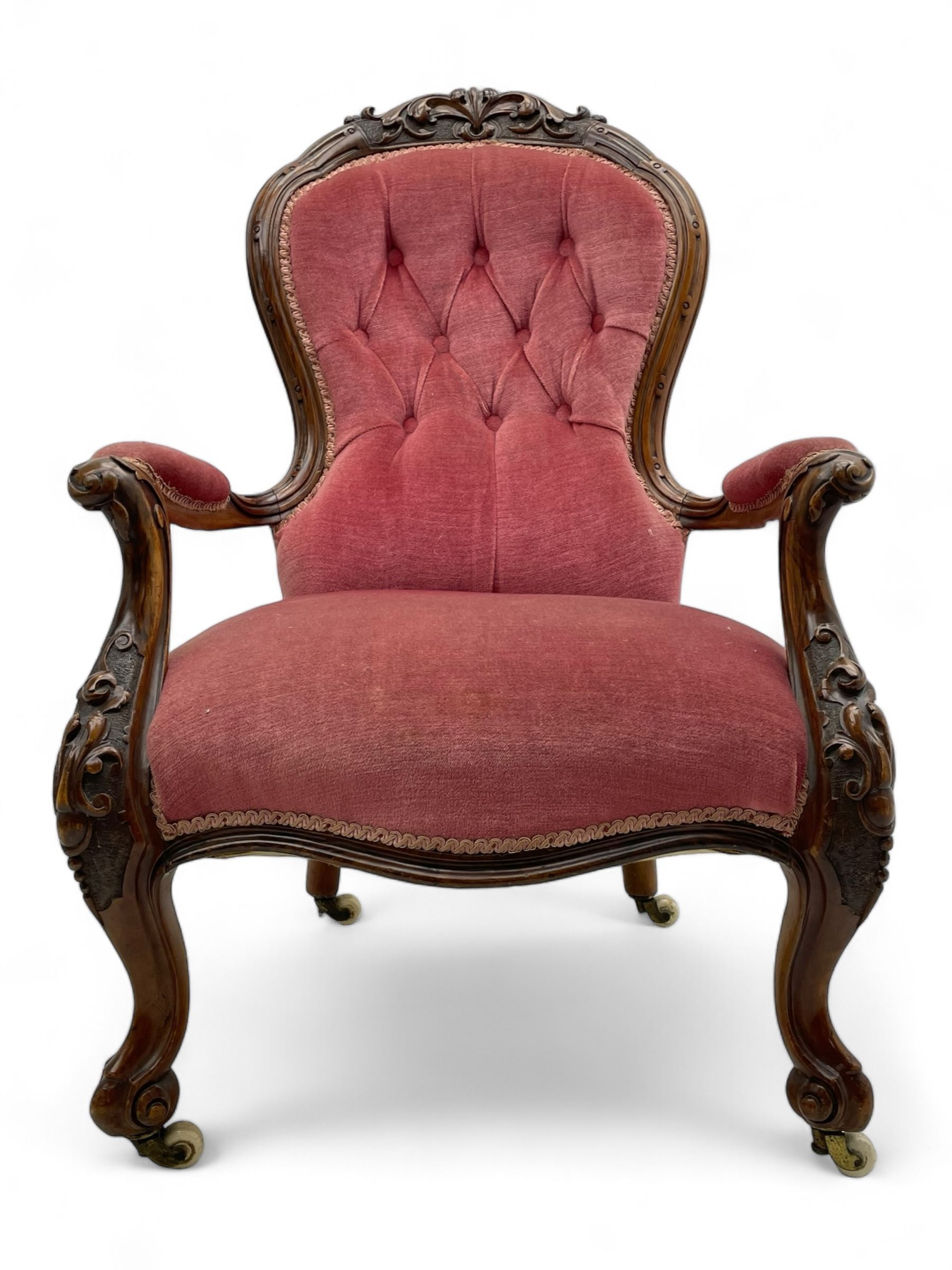 Victorian carved walnut open armchair, foliate carved cresting rail over butted back and sprung seat, upholstered in pink velvet scrolled arm terminals with moulded scrolling vines terminating to cabriole supports and ceramic castors