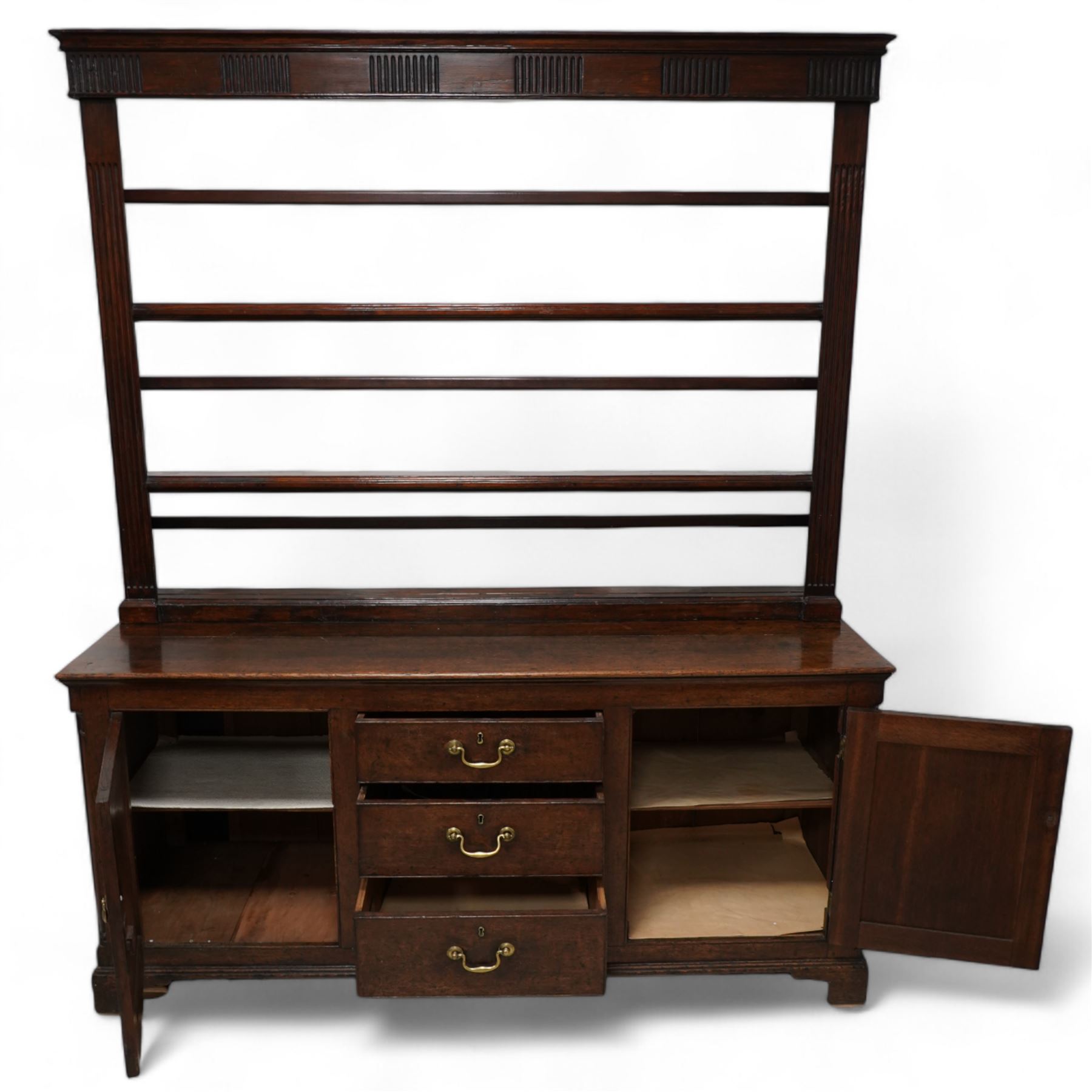 George III oak dresser, rectangular top, fitted with three central graduating cock-beaded drawers, flanked by panelled cupboards with quarter-canted pilaster uprights, lower moulded edge on bracket feet; with associated stained pine plate rack, carved with fluted detail (W170cm H124cm)